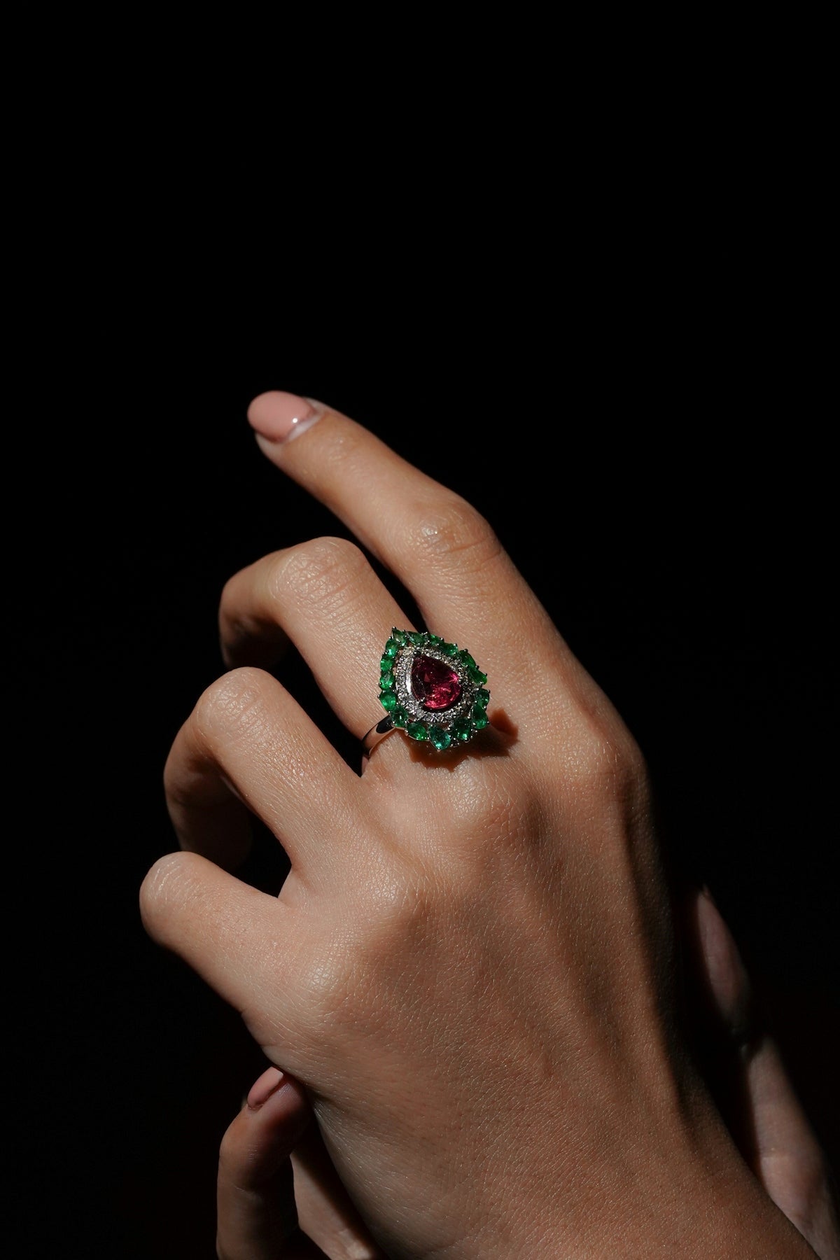 A hand wearing a large red and green gemstone ring.