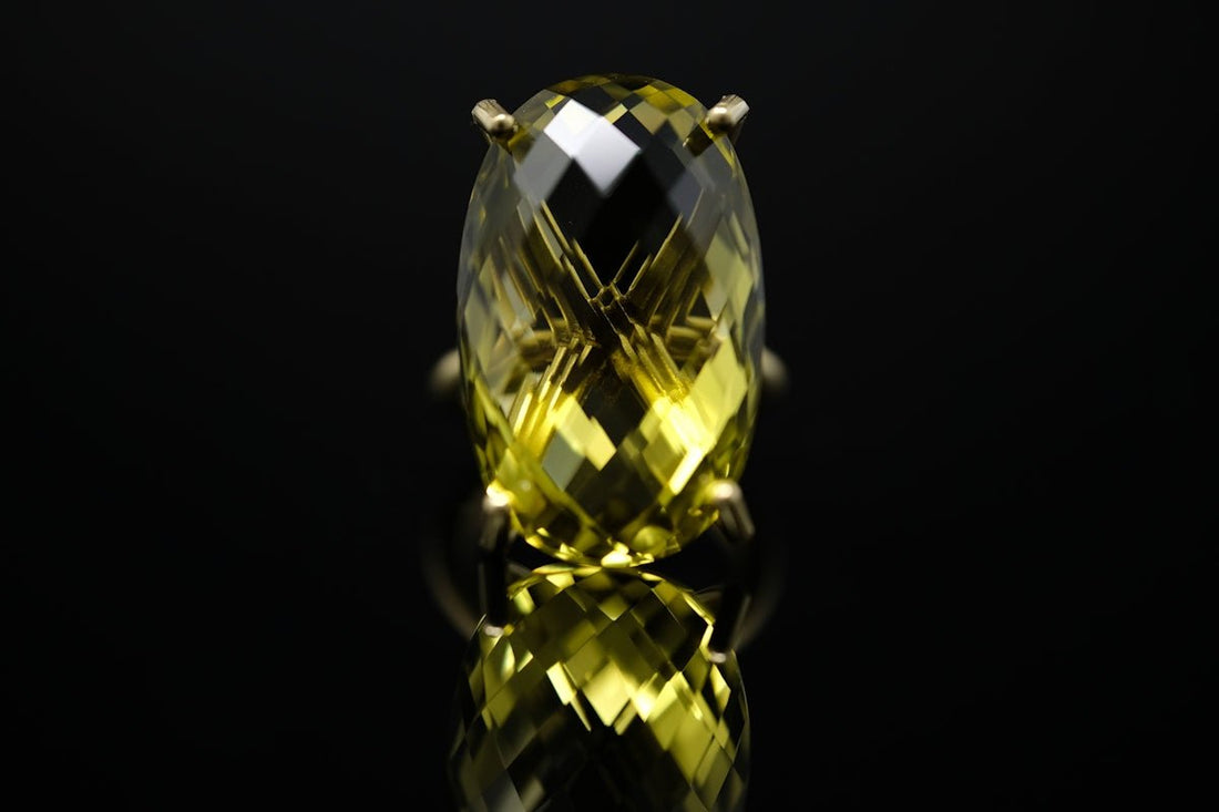 A faceted yellow gemstone ring reflecting on a black surface