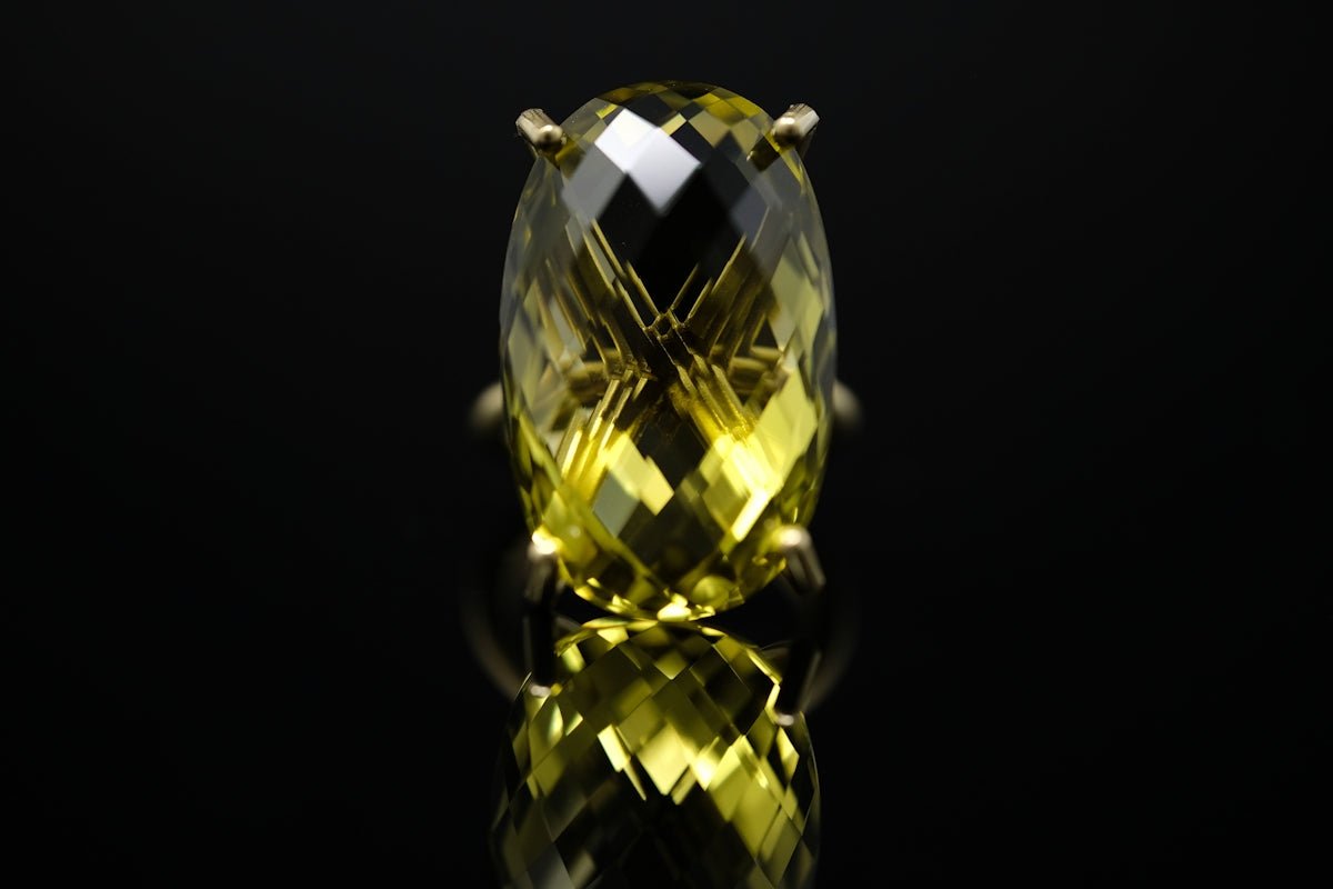 A faceted yellow gemstone ring reflecting on a black surface
