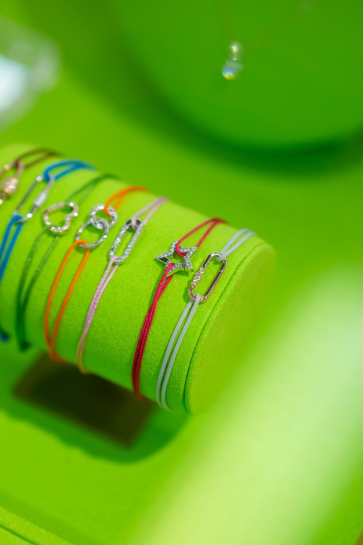 Bracelets with colorful strings sit on a green display.