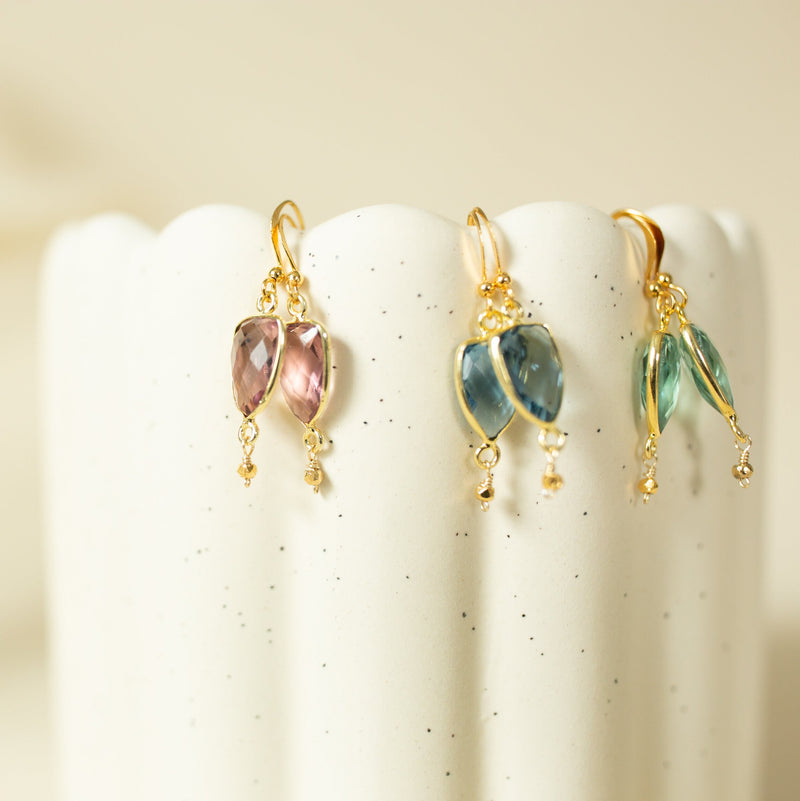 A pair of gold earrings with gemstones, displayed on a white speckled surface.