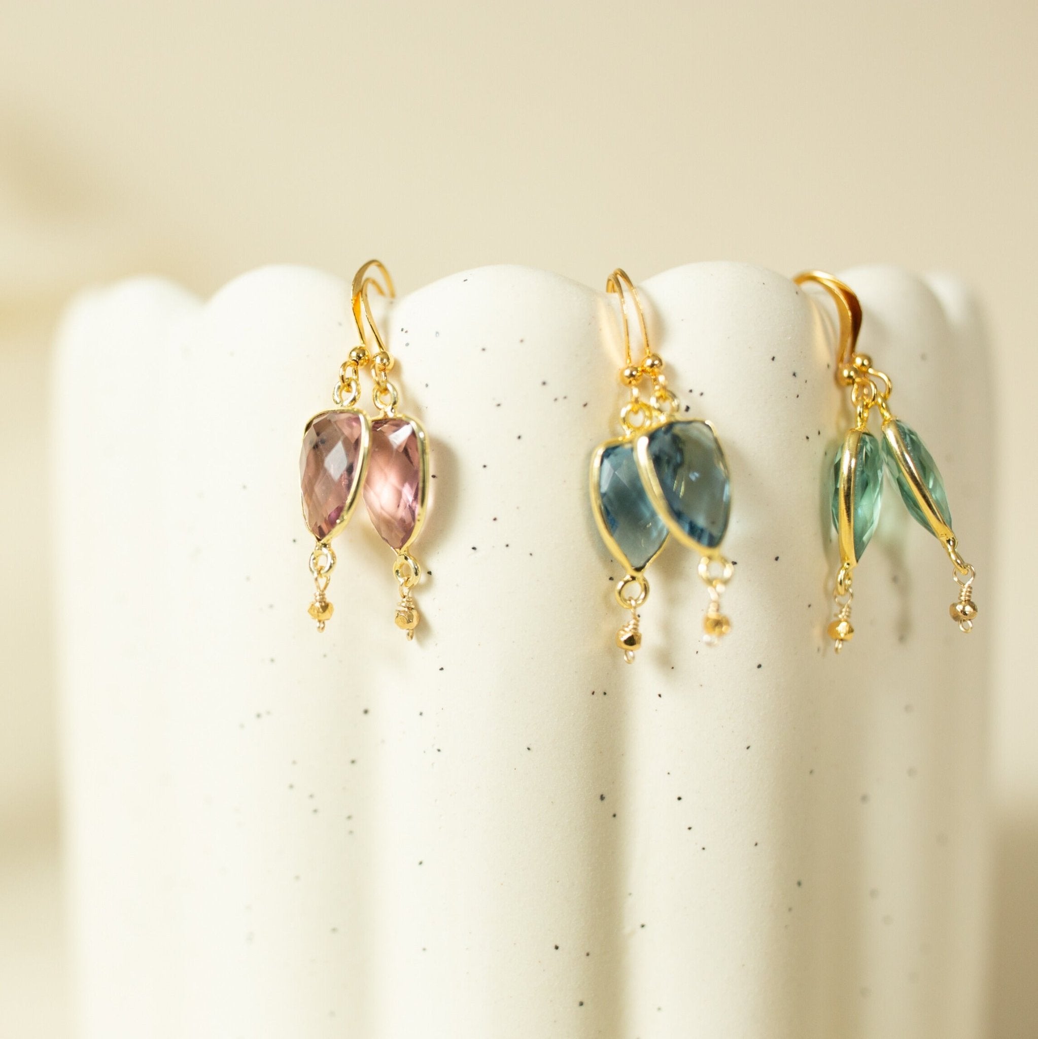 A pair of gold earrings with gemstones, displayed on a white speckled surface.