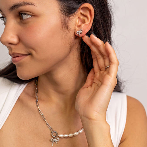 A woman is wearing a necklace with a pendant and earrings, smiling and looking to the side.