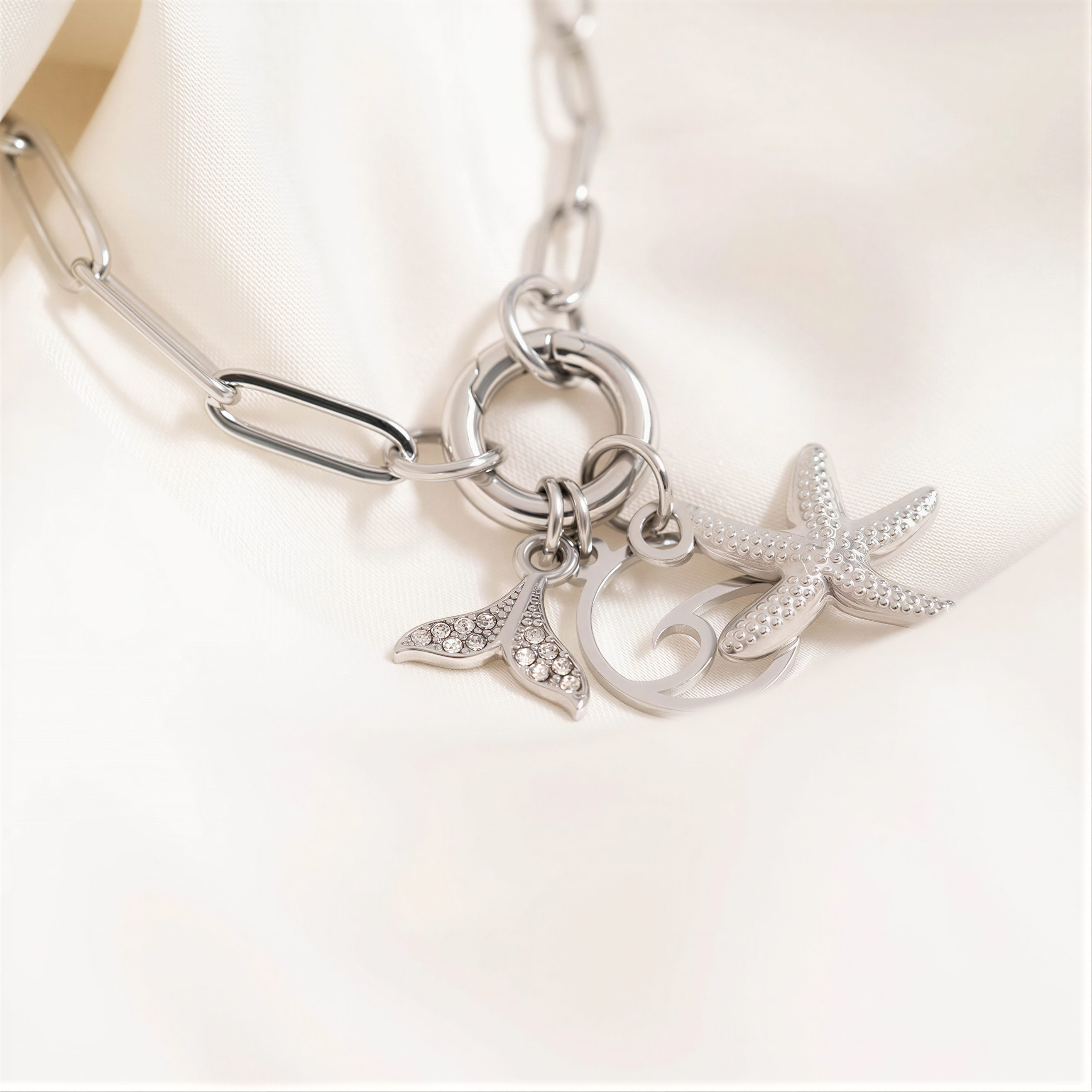 A silver necklace with a charm featuring a mermaid tail and starfish.