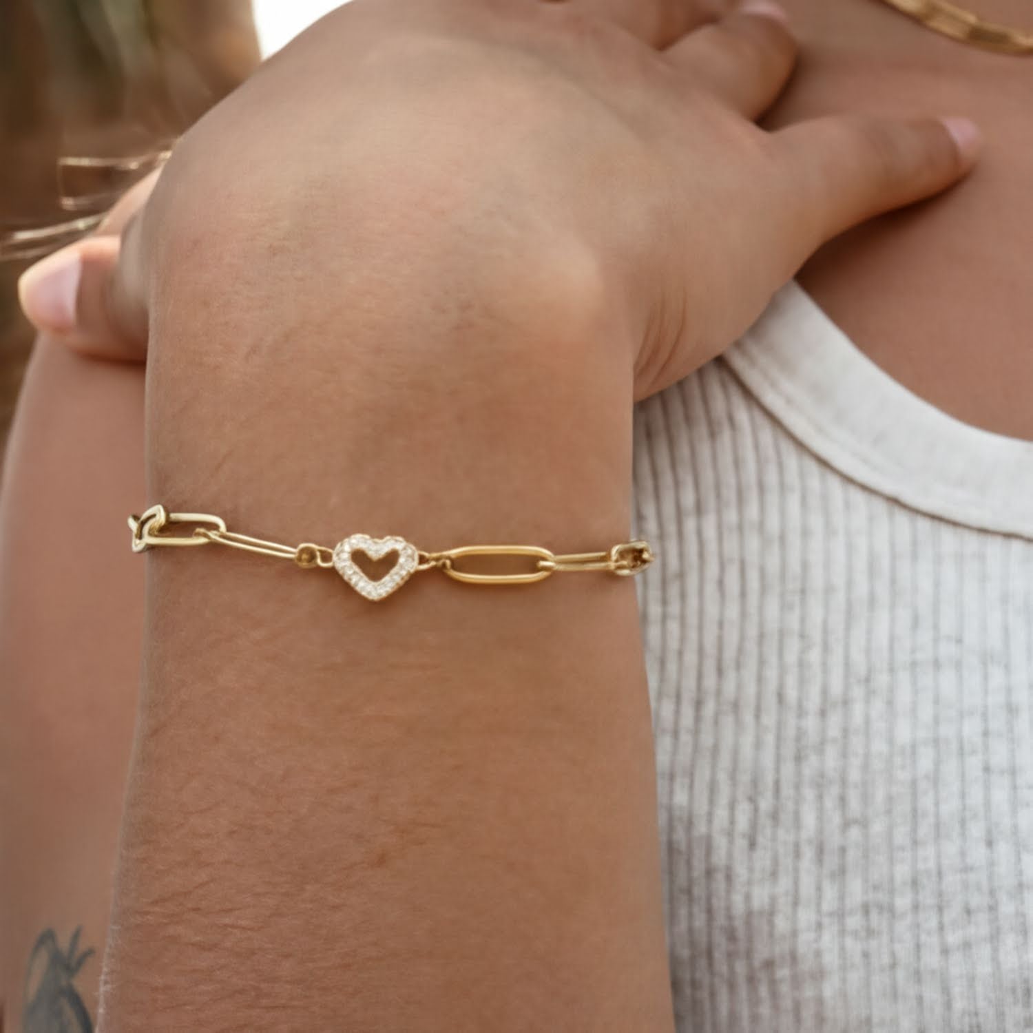 A close-up view of a person's wrist wearing a gold-colored bracelet with a heart-shaped charm.