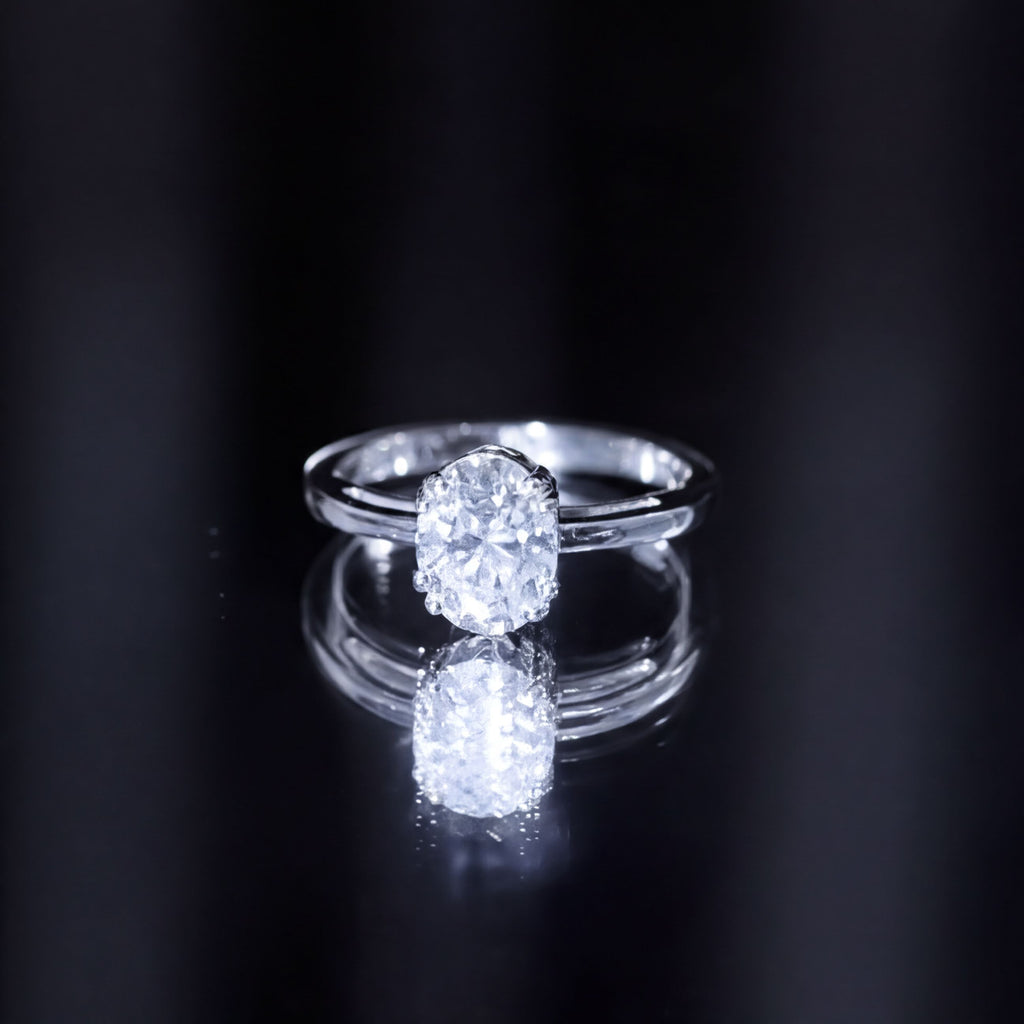 A close-up of a diamond engagement ring with a large central diamond set in a silver band, reflecting on a dark surface.