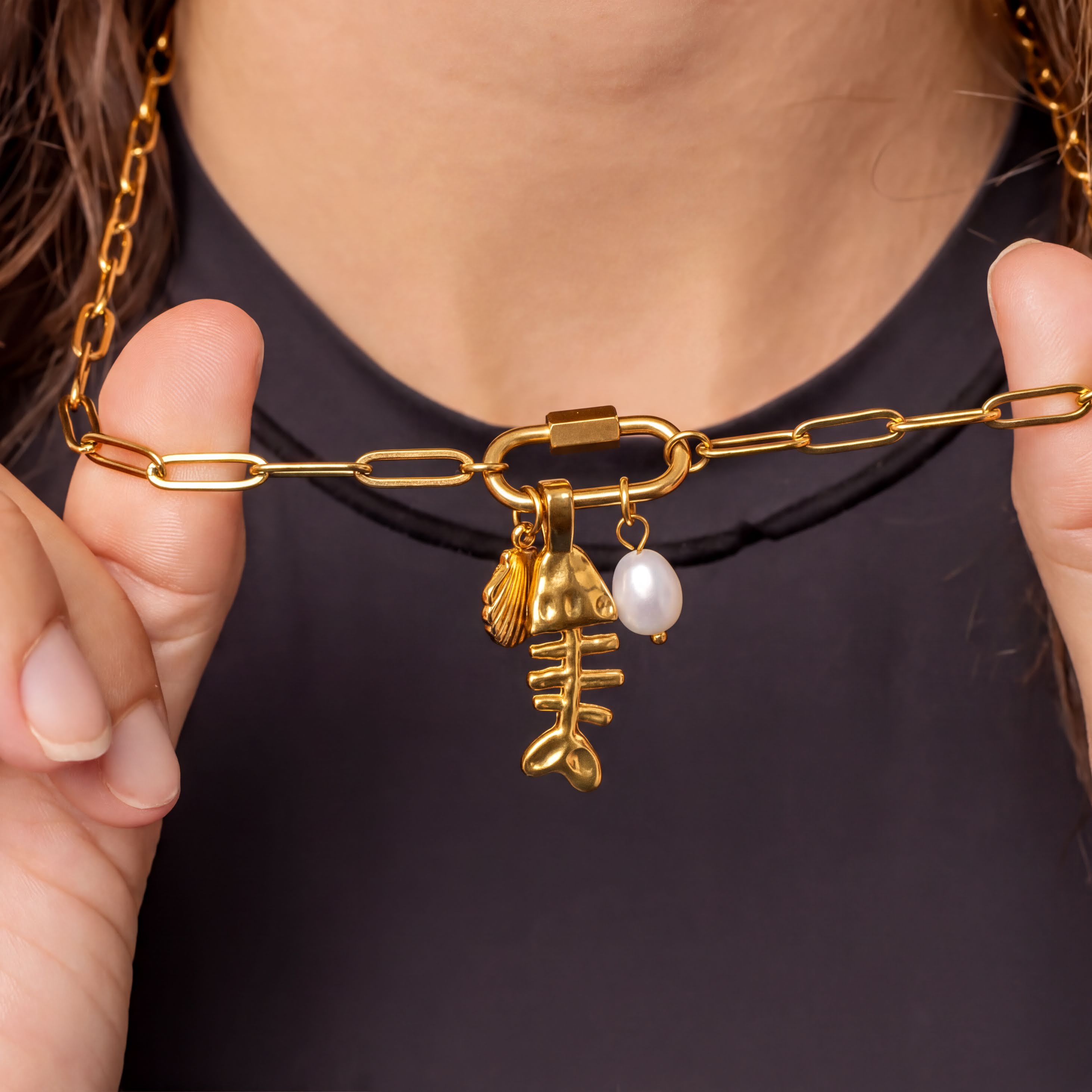 A close-up view of a person's neck and chest wearing a gold-colored necklace with a pendant featuring a fish design and a pearl.
