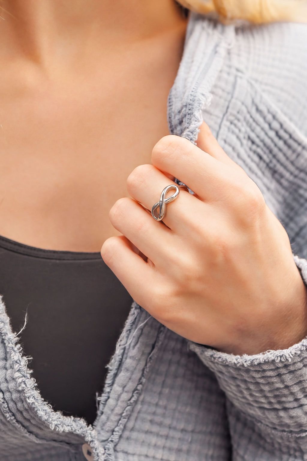 A close-up of a person's hand wearing a silver ring, with a gray sweater partially visible underneath.