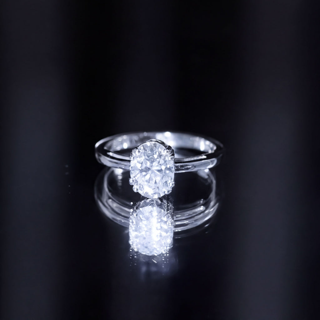 A close-up of a diamond engagement ring with a large central diamond set in a silver band, reflecting on a dark surface.