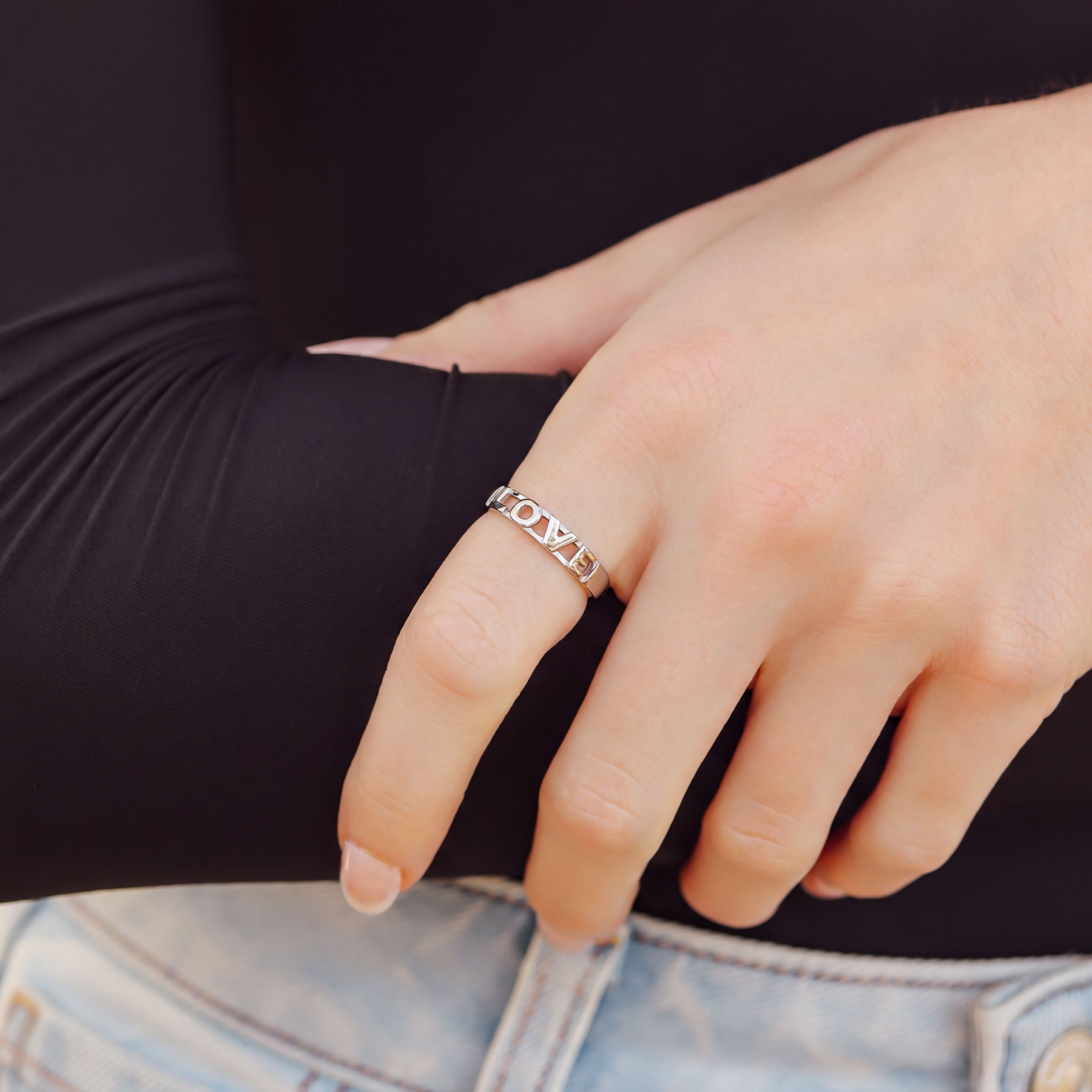 A close-up of a person's hand wearing a ring with the word "MOM" engraved on it.