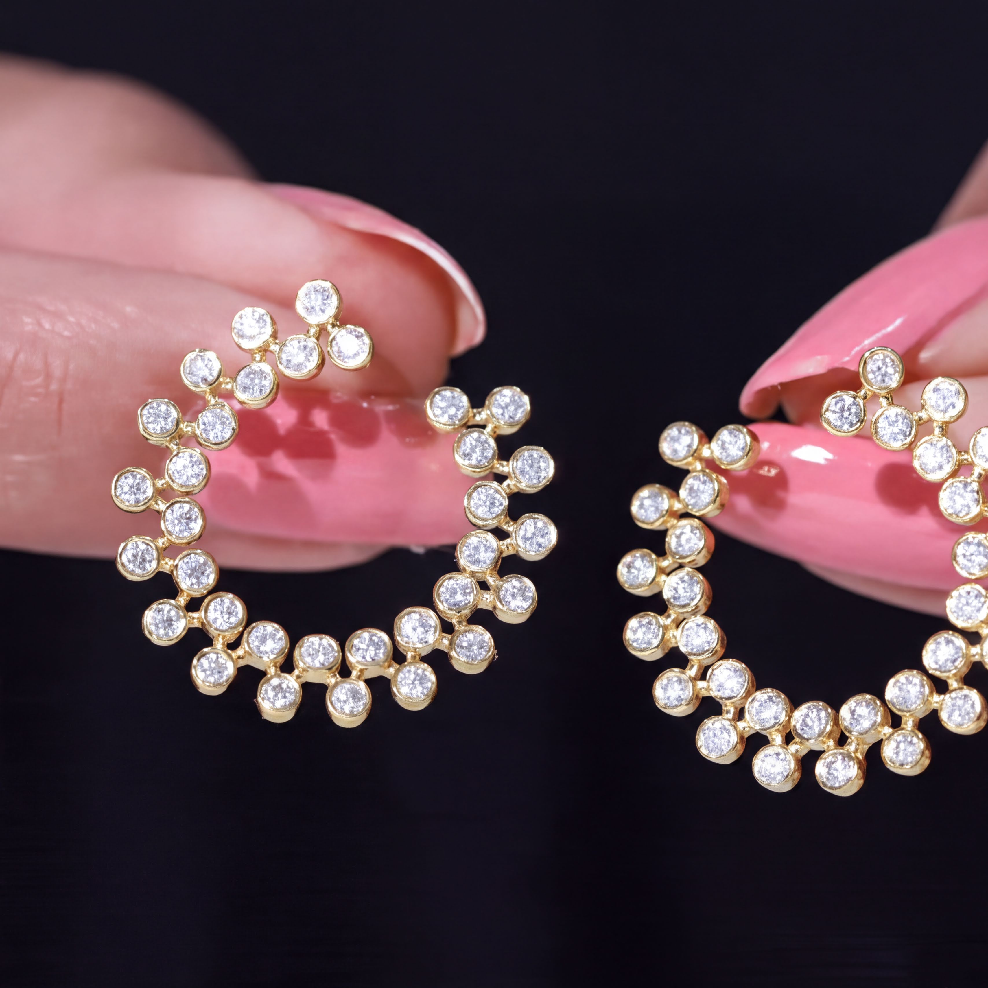 A close-up of a person's hand holding a pair of gold earrings with small diamonds on them.