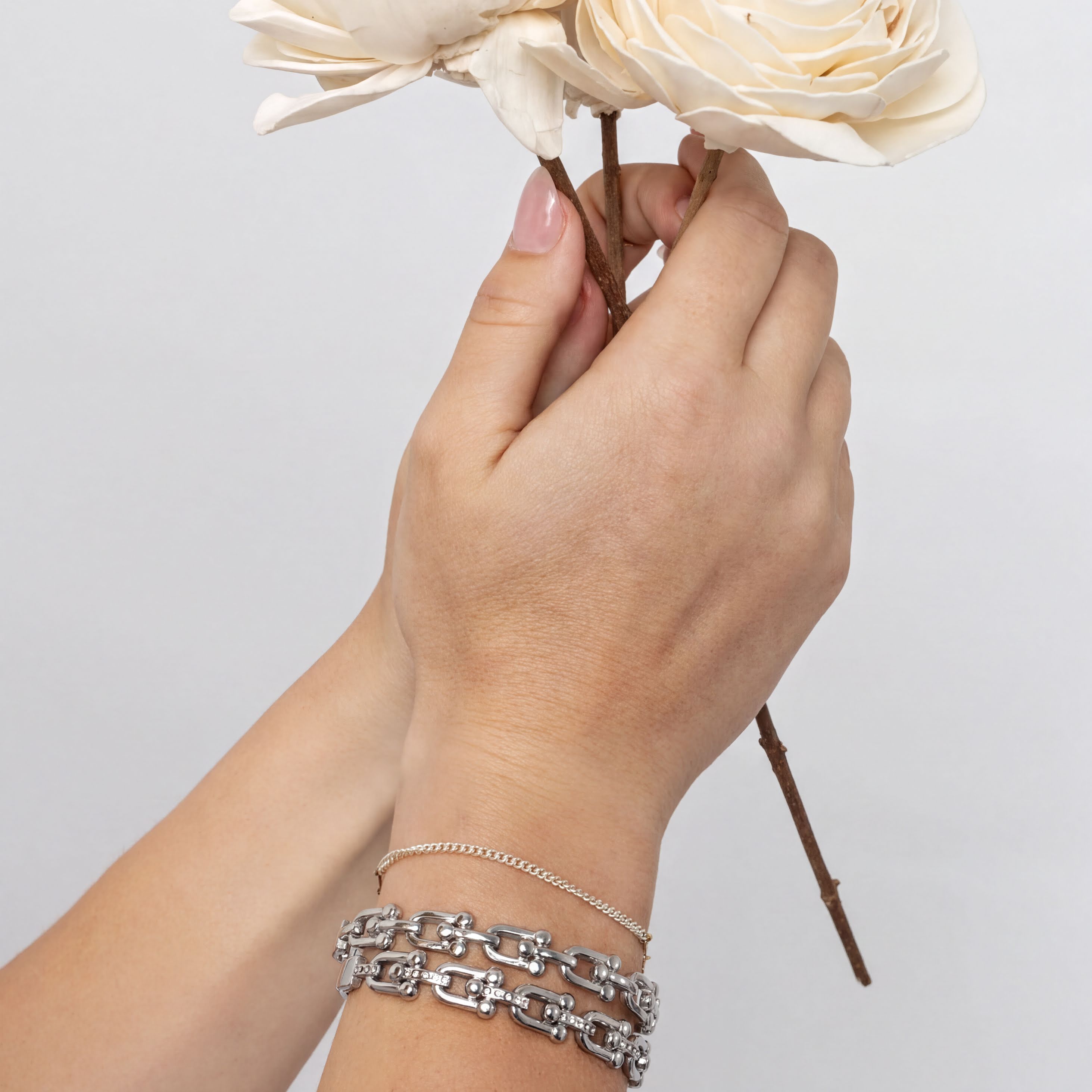 Hand holding a bouquet of flowers with silver bracelets on a plain background