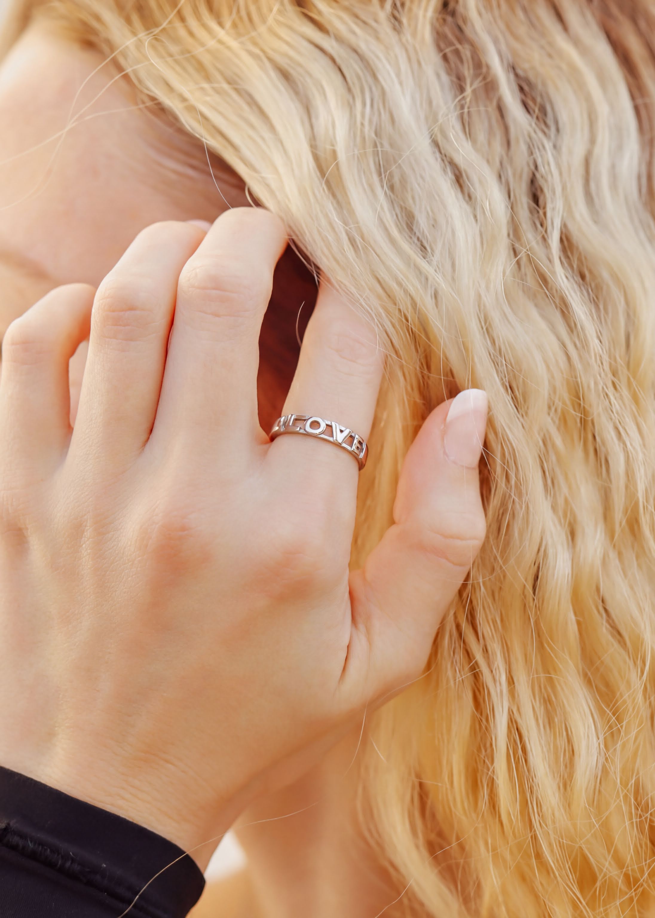 A close-up of a person's hand wearing a ring, with their hair visible behind them.