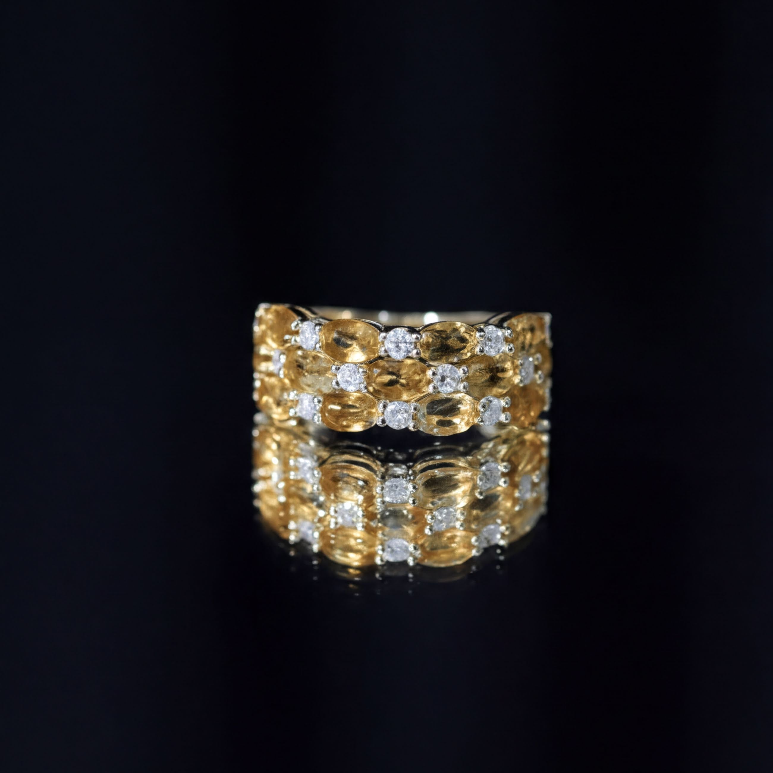 A gold ring with a diamond band is displayed against a black background, reflecting the ring on a surface below.