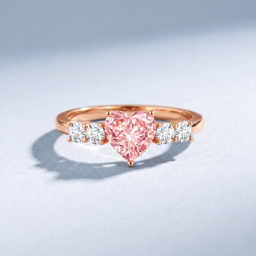 A pink diamond ring with a heart-shaped center stone and three smaller diamonds on either side.
