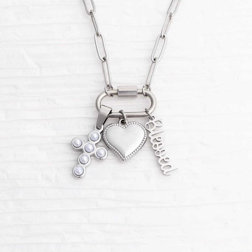 Silver necklace with heart, cross, and 'blessed' charm on a white background