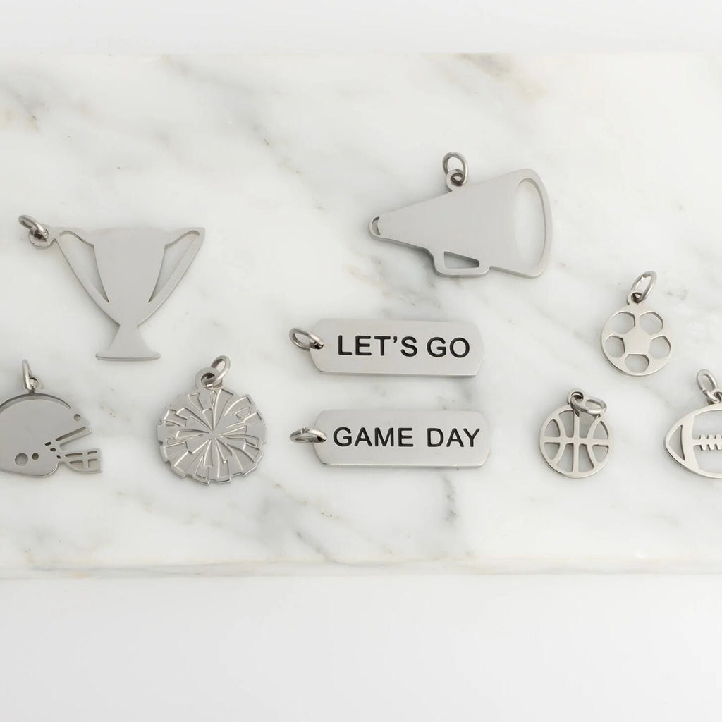 Collection of silver charms including a megaphone, football, and 'Let's Go Game Day' text on a marble surface.