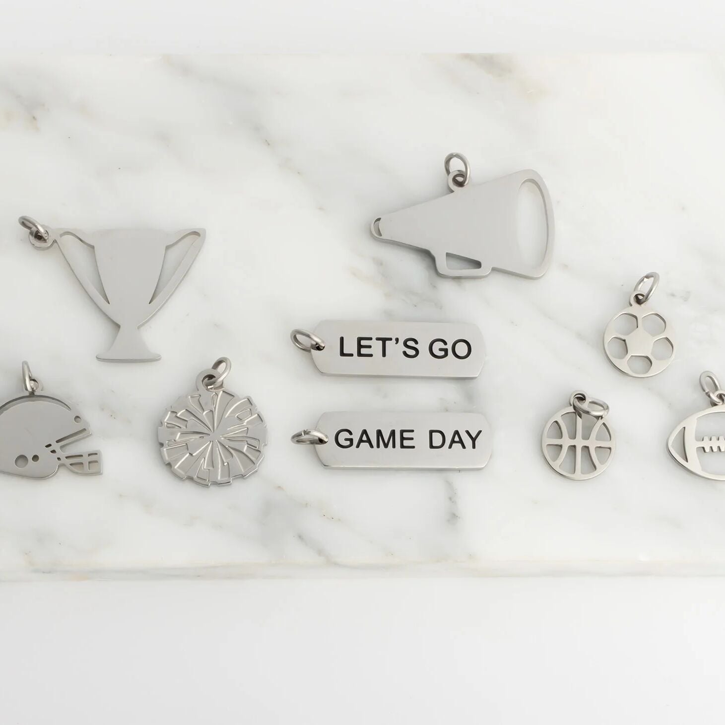 Collection of silver charms including a megaphone, football, and 'Let's Go Game Day' text on a marble surface.