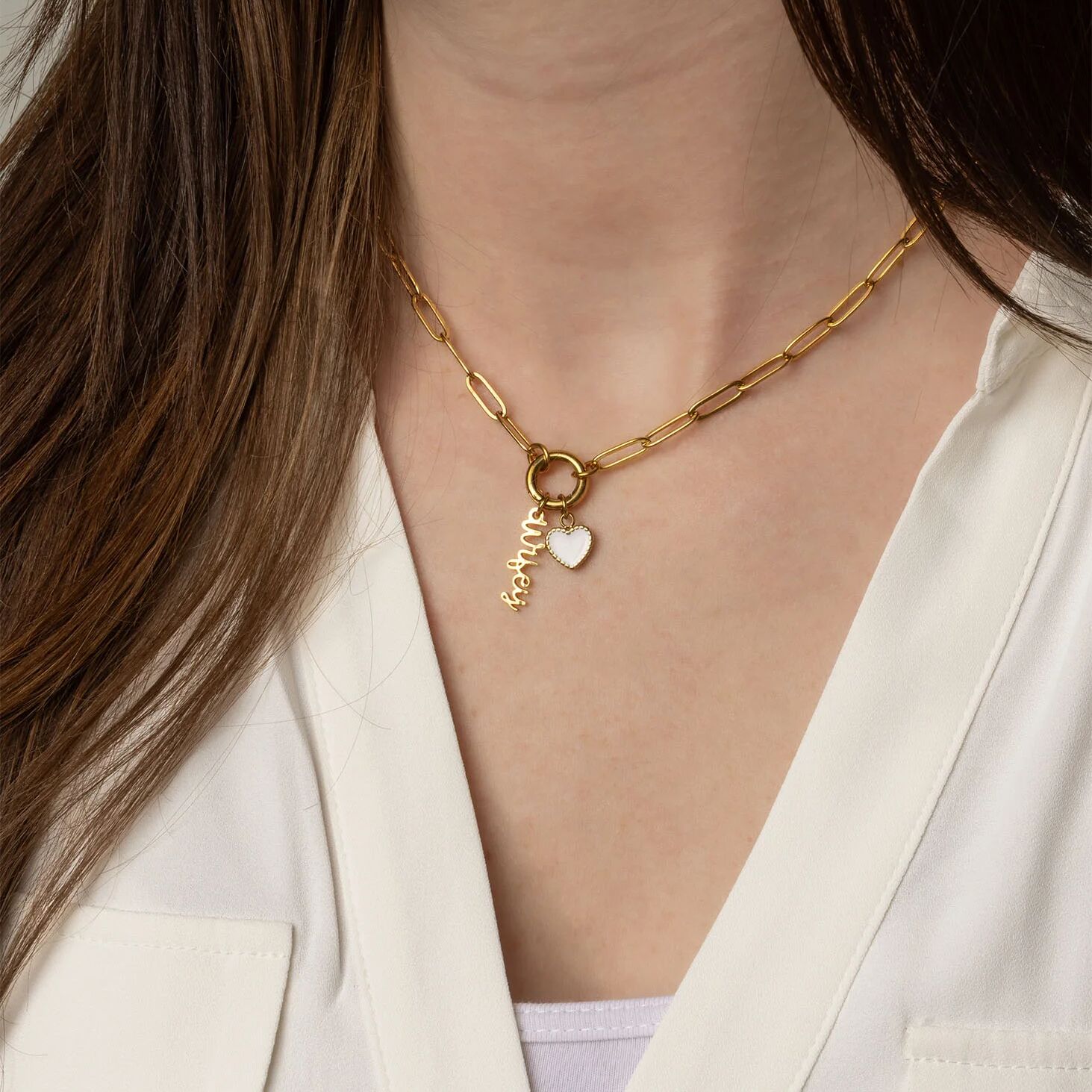 Gold necklace with heart and name charm worn by a person in a white outfit.