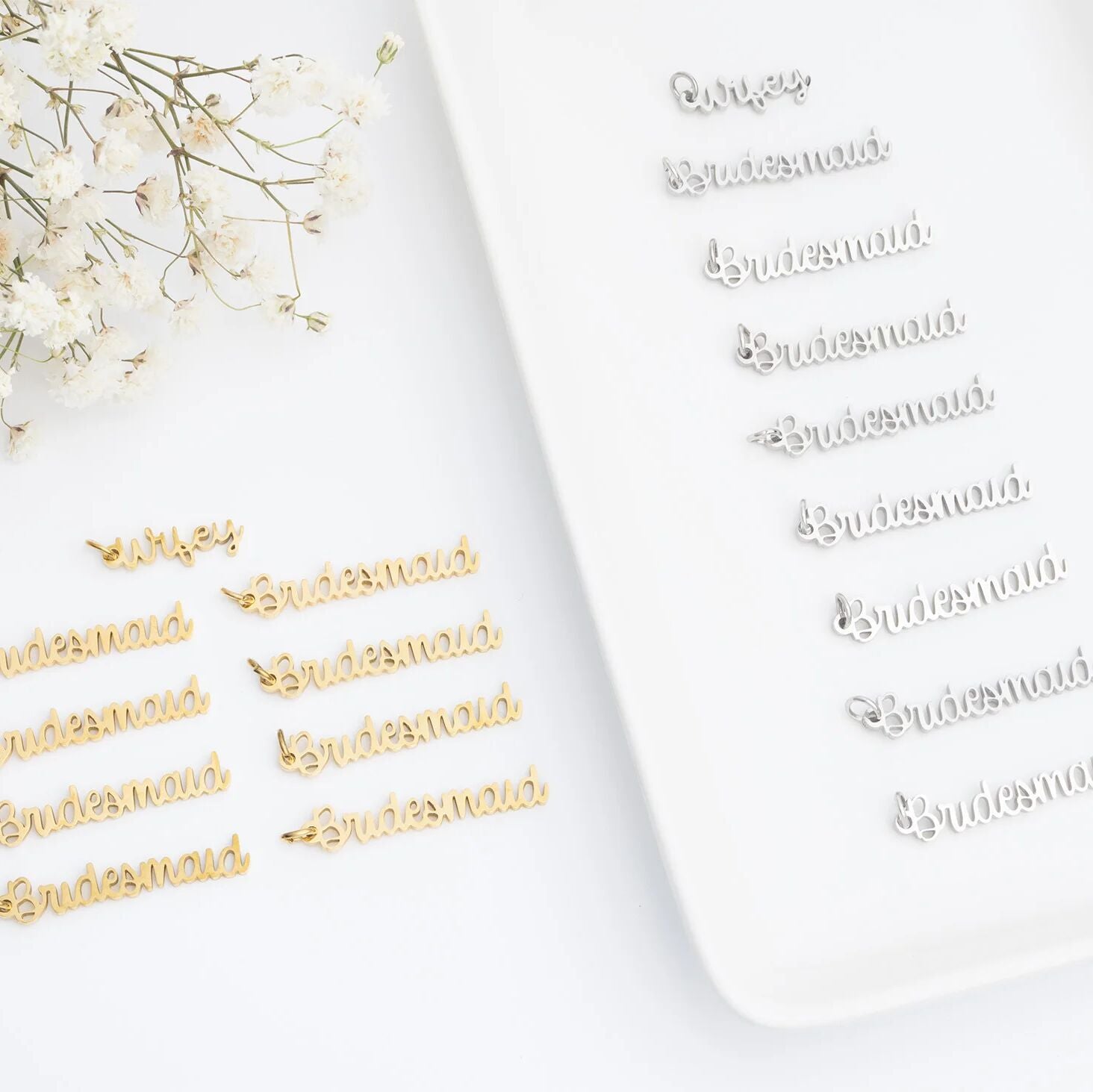 Gold 'Bridesmaid' pins on a white surface with baby's breath flowers.