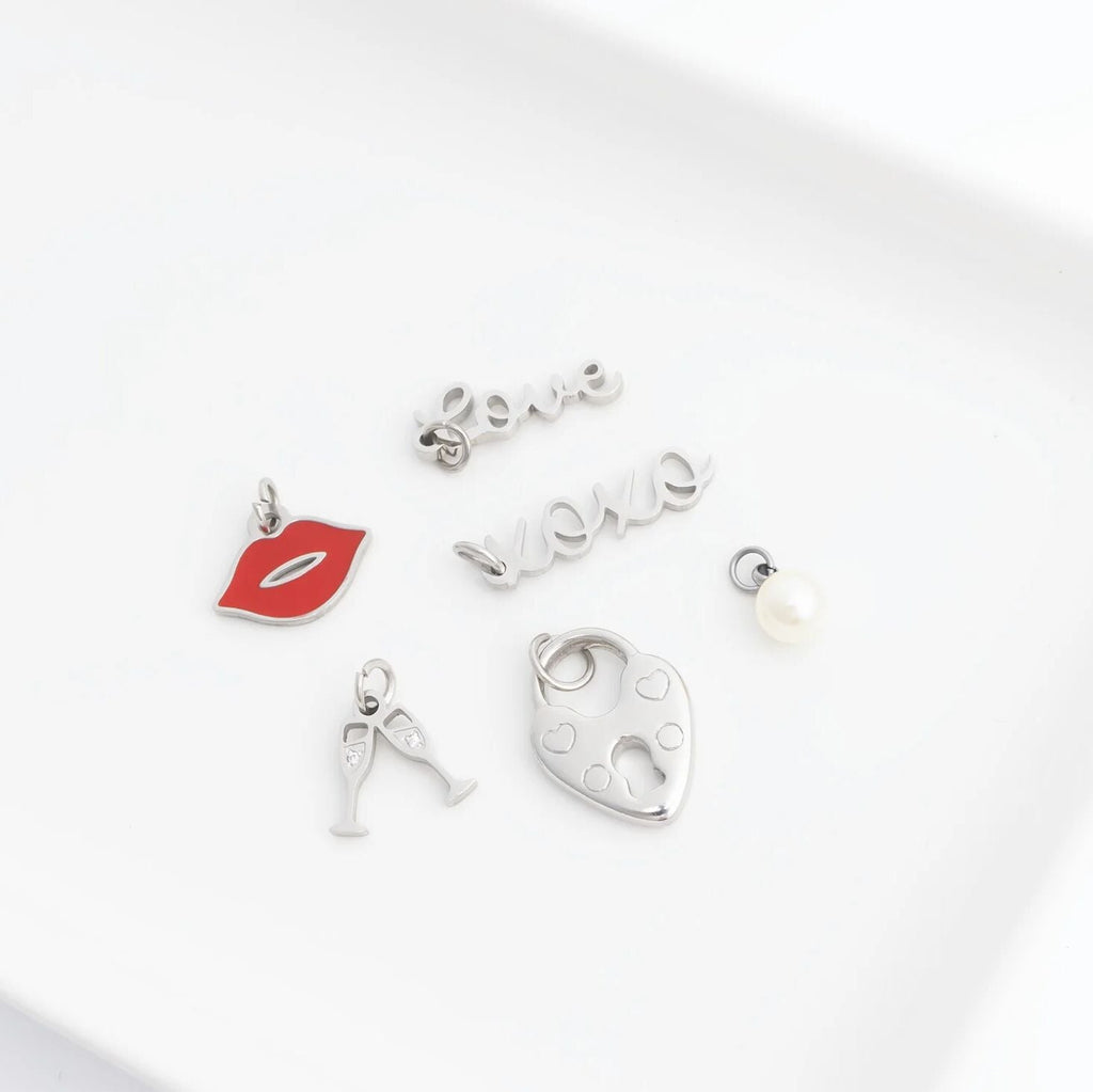 Collection of silver charms including a red lip, letter 'A', heart, and pearl on a white background