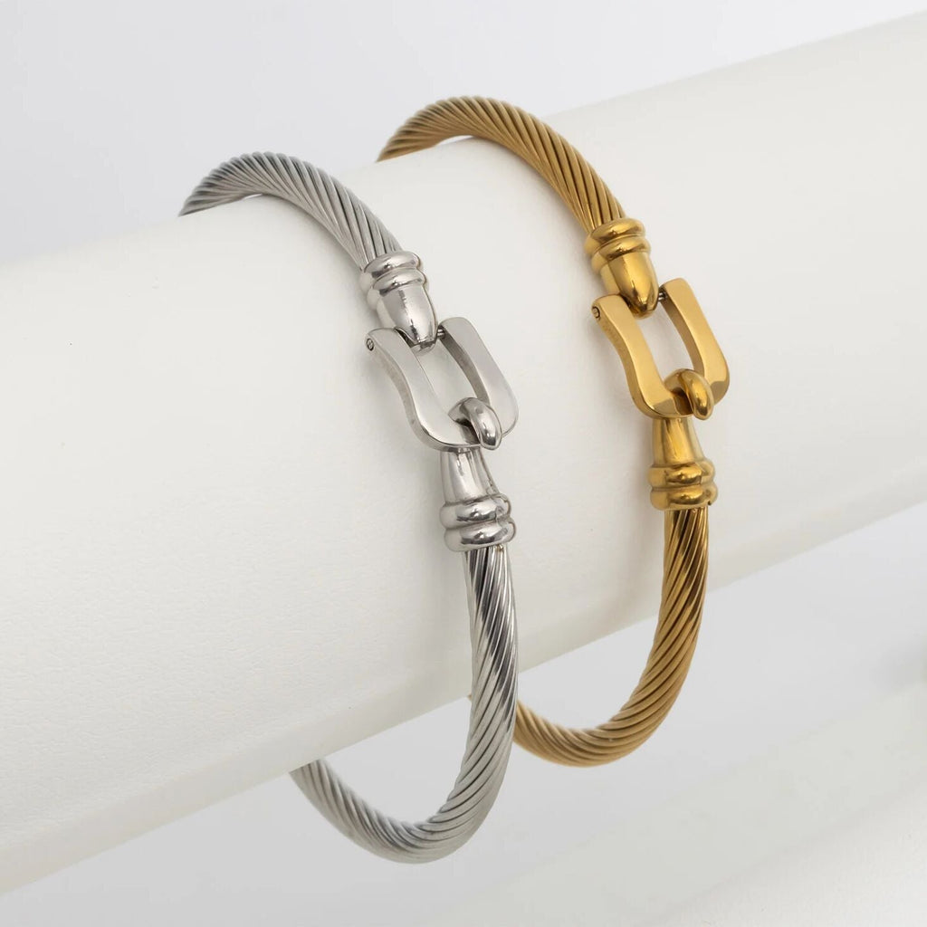 Two metallic buckle clasp bracelets, one silver and one gold, on a white surface.