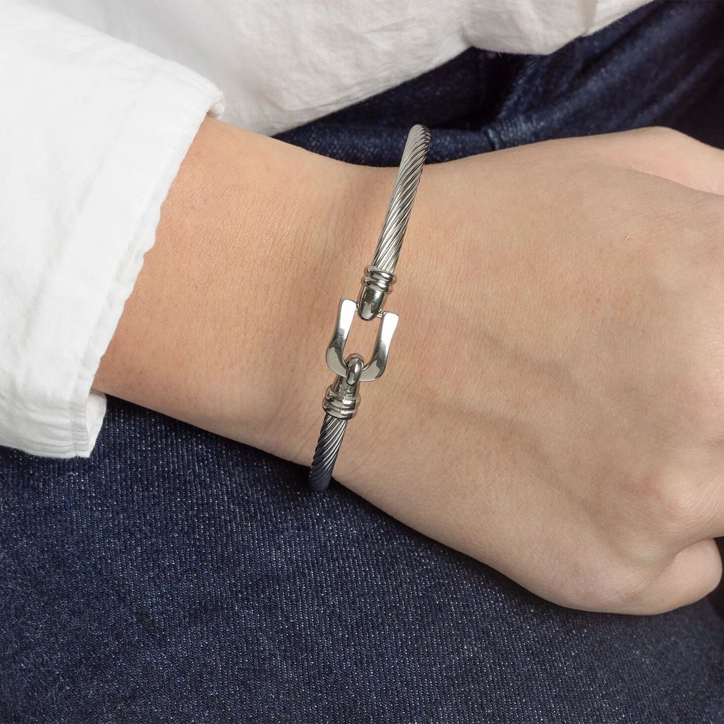 Silver bracelet with a buckle clasp on a wrist against a dark fabric background