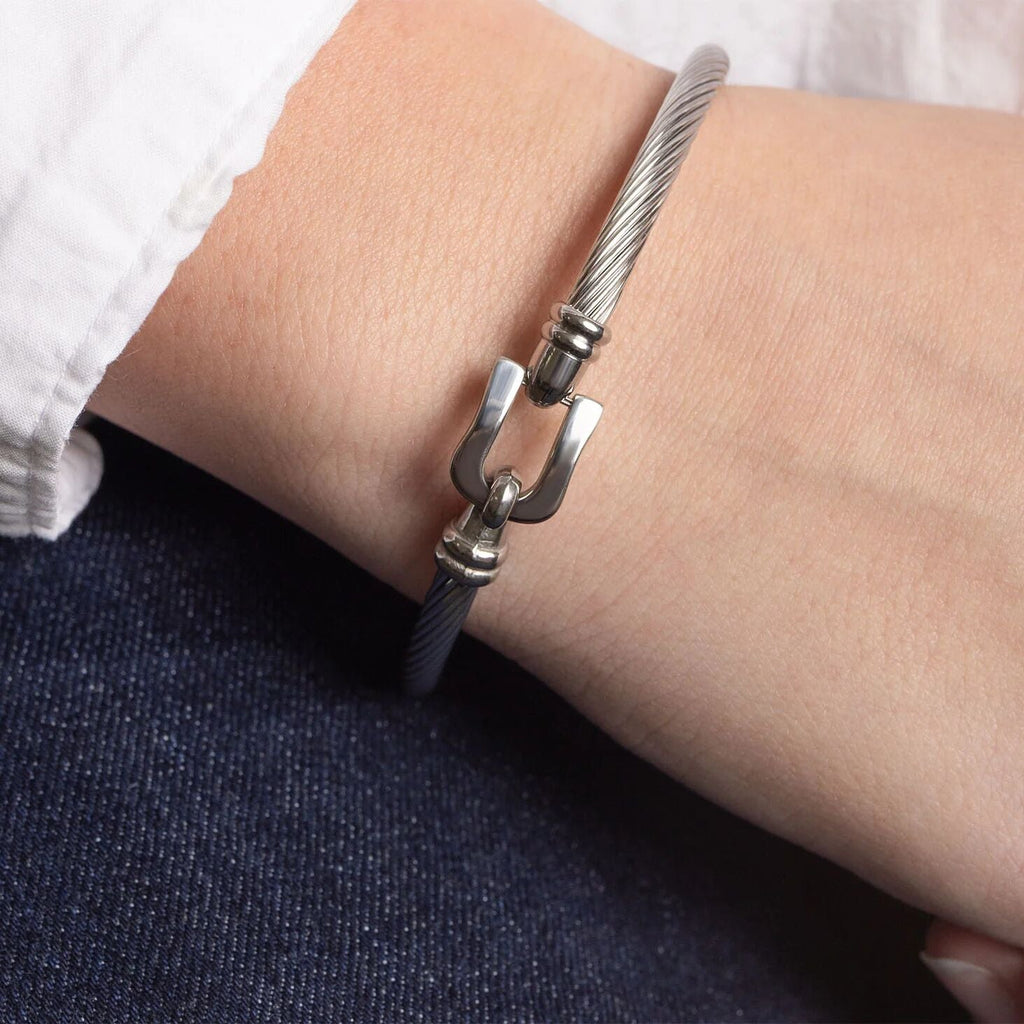 Silver bracelet with a buckle clasp on a wrist against a white shirt and dark jeans background