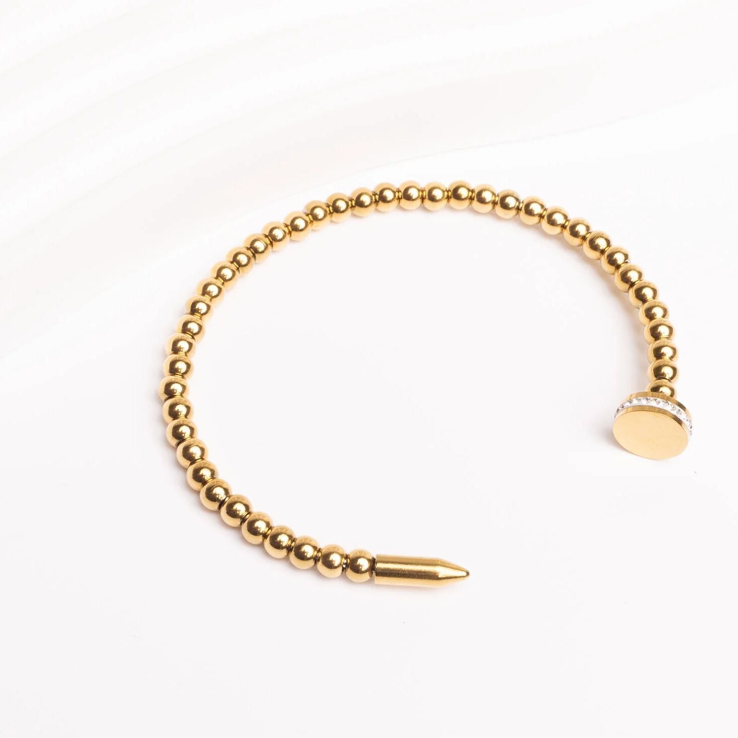Gold beaded bracelet with a bullet-shaped clasp on a white background