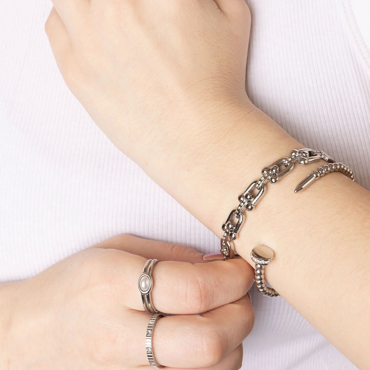 Close-up of a wrist wearing a silver bracelet and rings on a white background