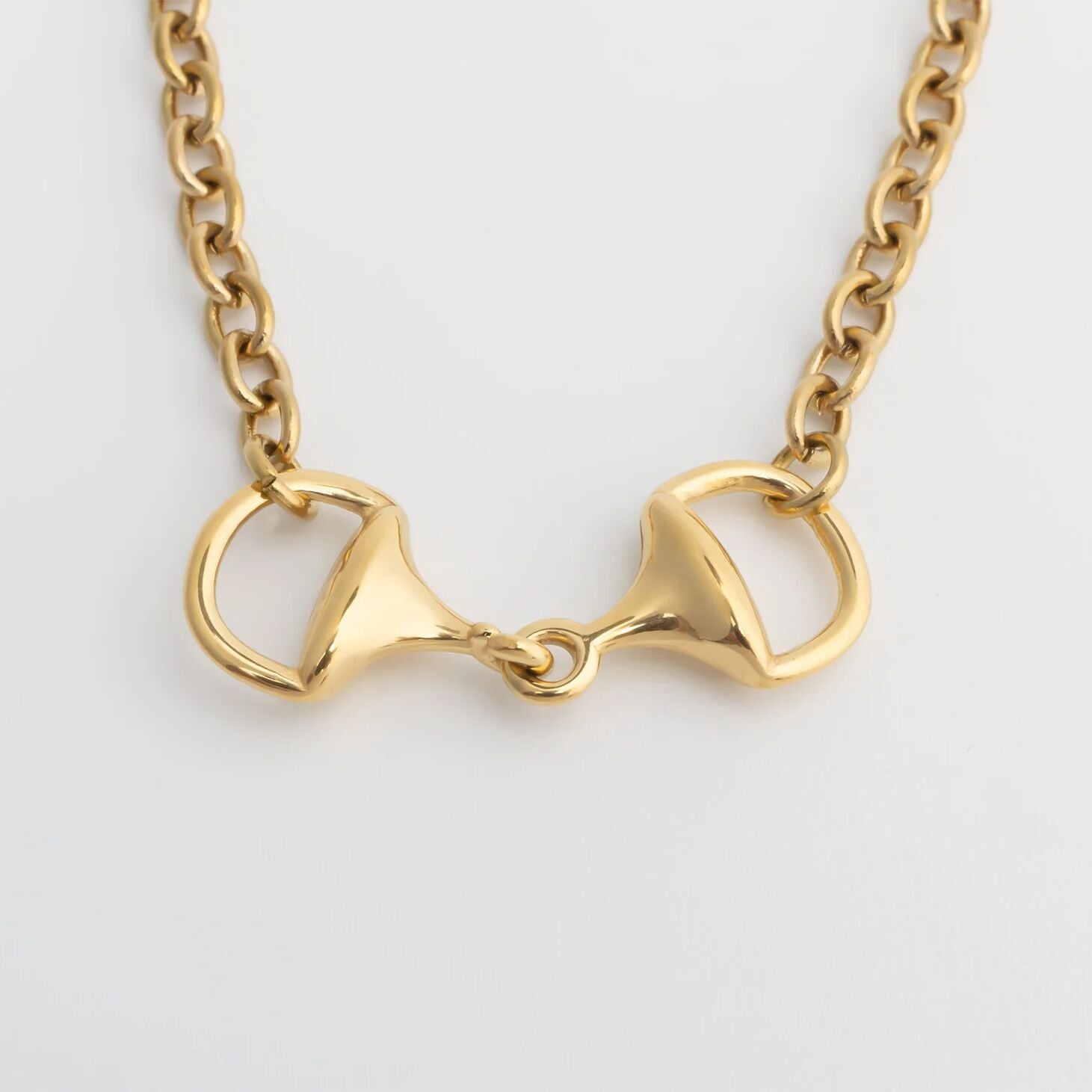 Gold bracelet with a horse bit pendant on a light gray background