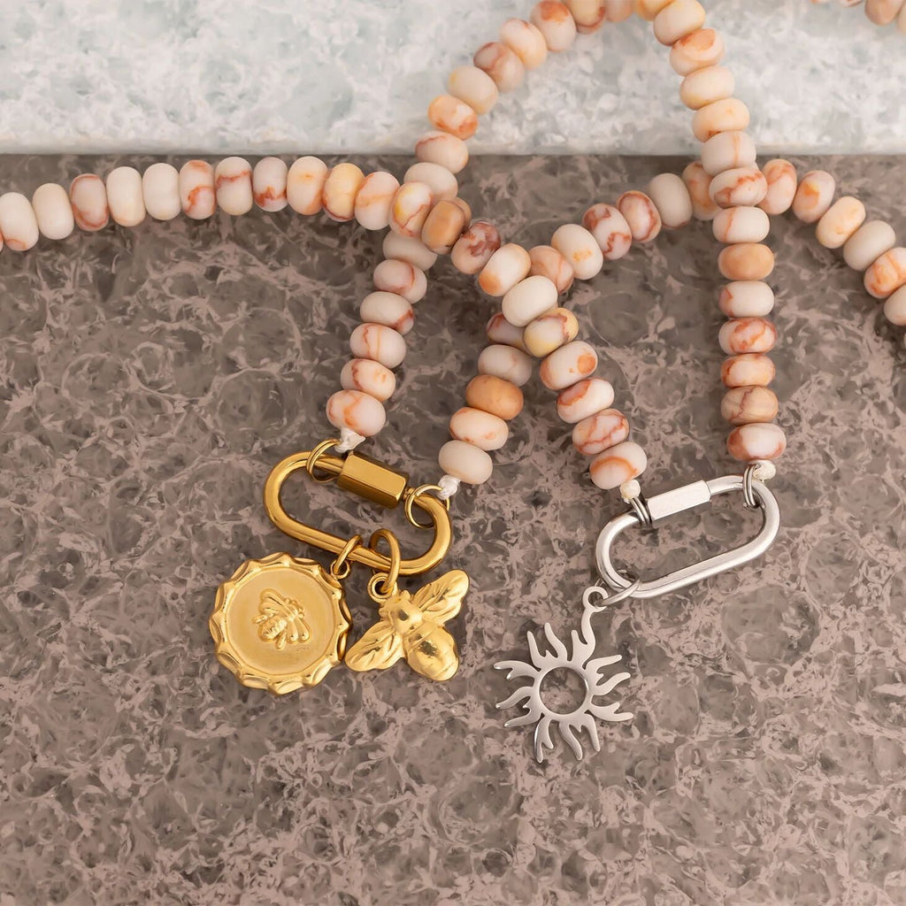 Necklace with pink beads and gold and silver charms on a textured surface