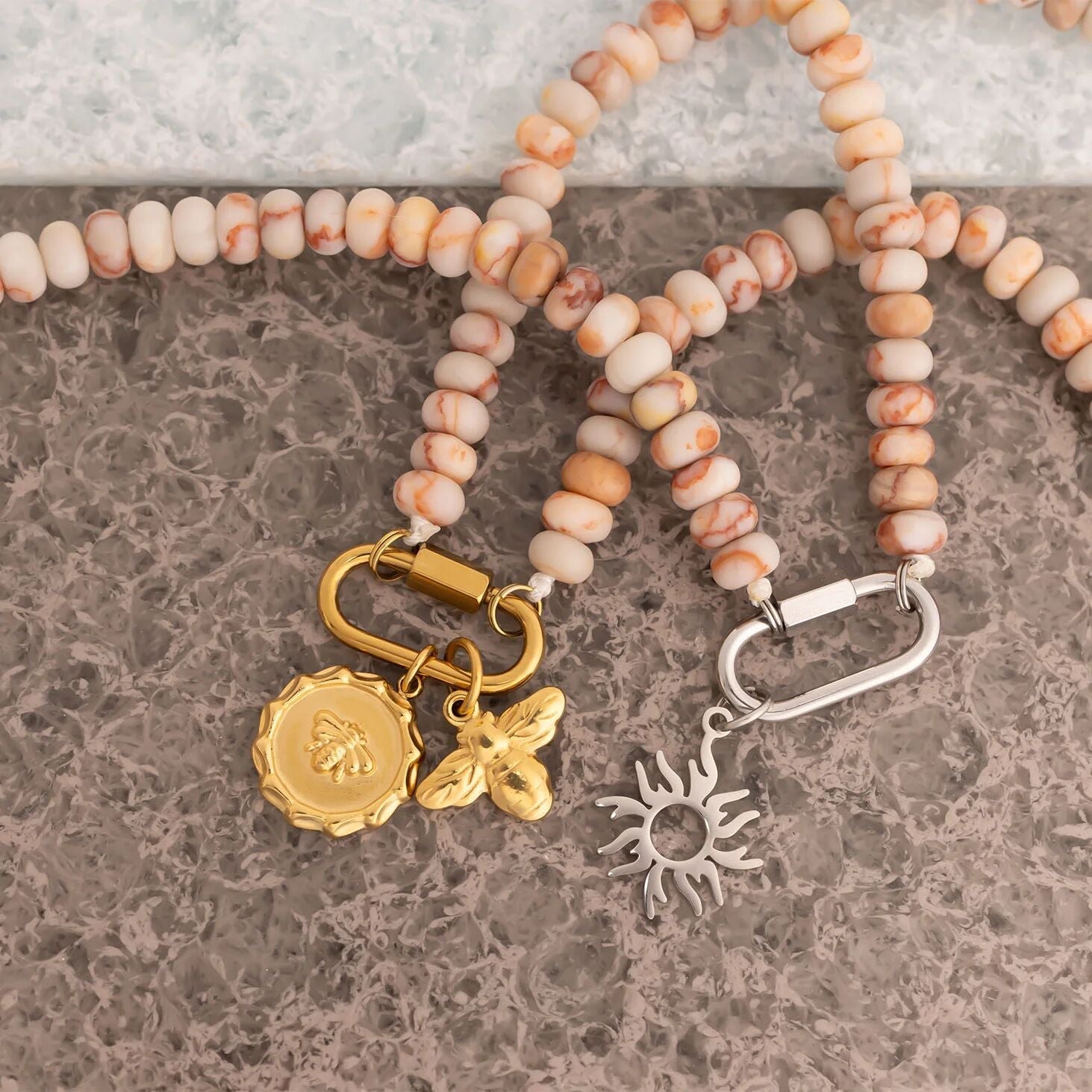 Necklace with pink beads and gold and silver charms on a textured surface