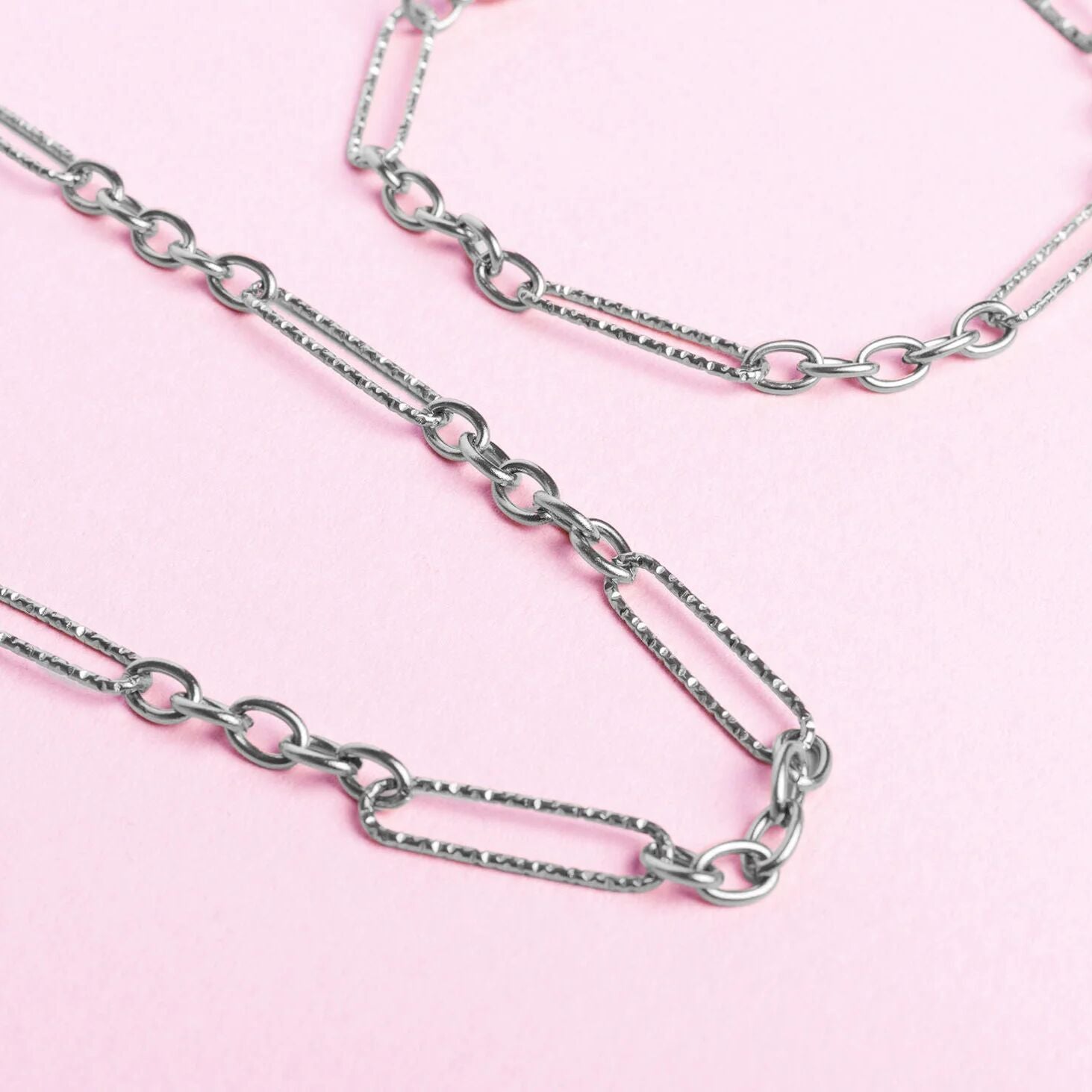 Silver chain necklaces on a pink background