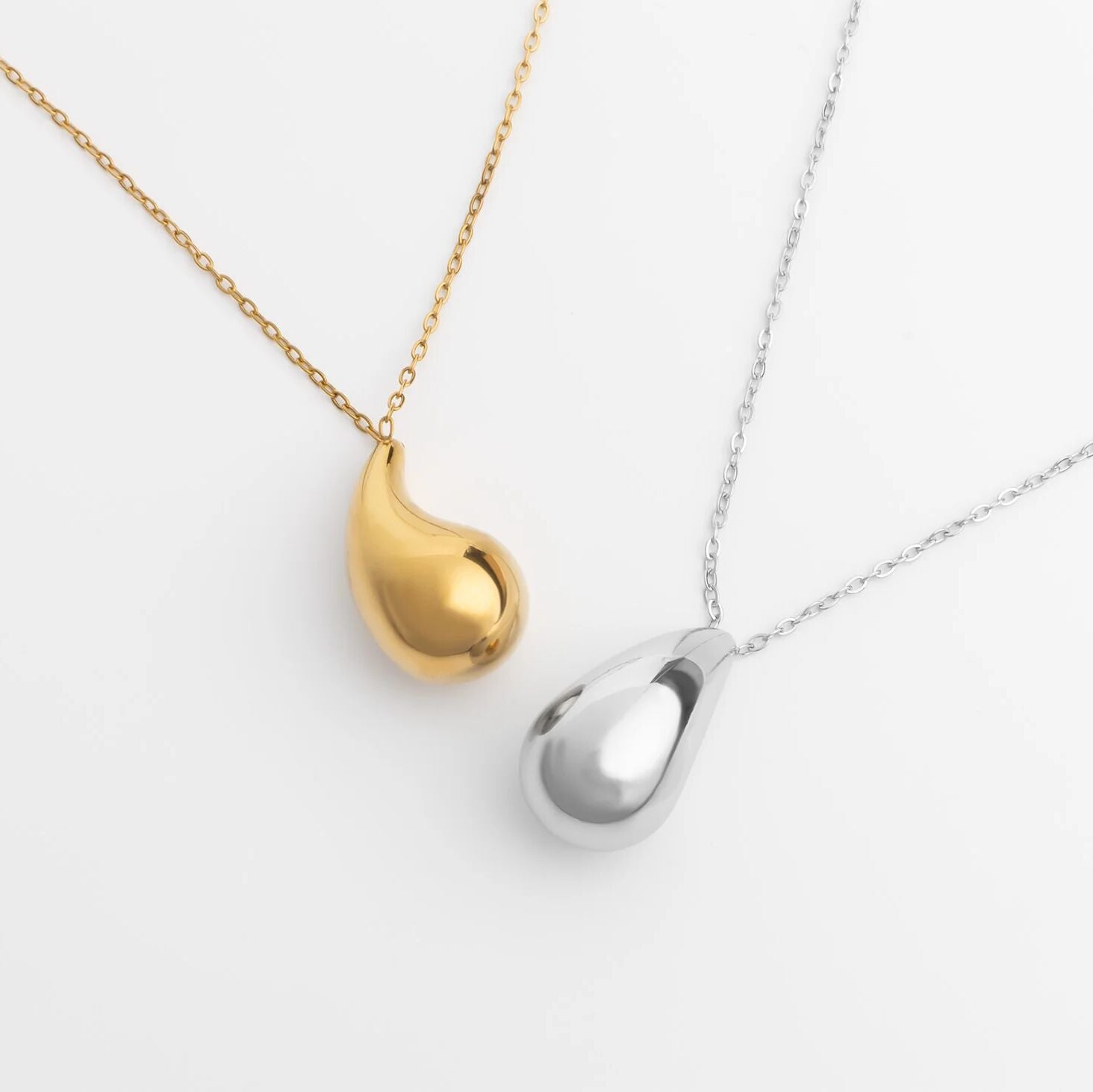 Gold and silver teardrop-shaped pendants on chains against a white background