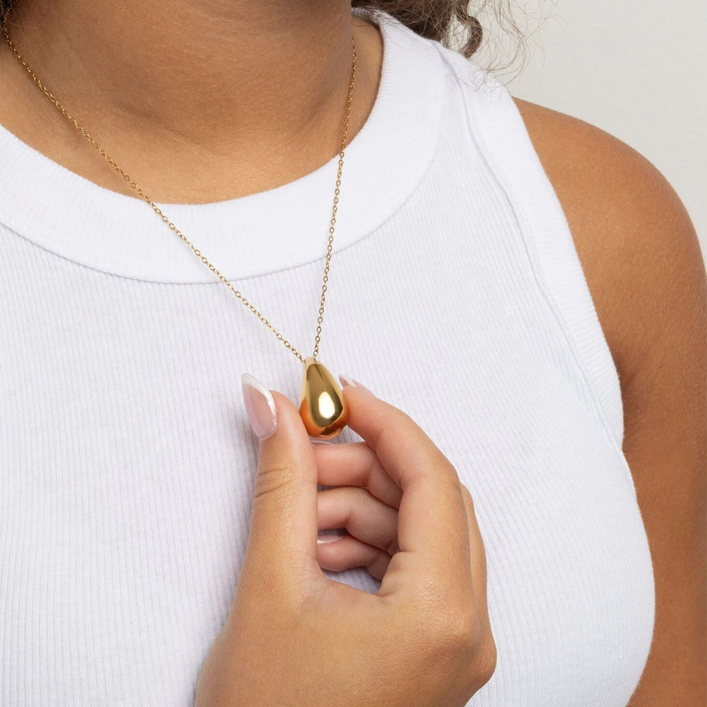 Gold Tear Drop Charm Necklace held by a hand against a white background