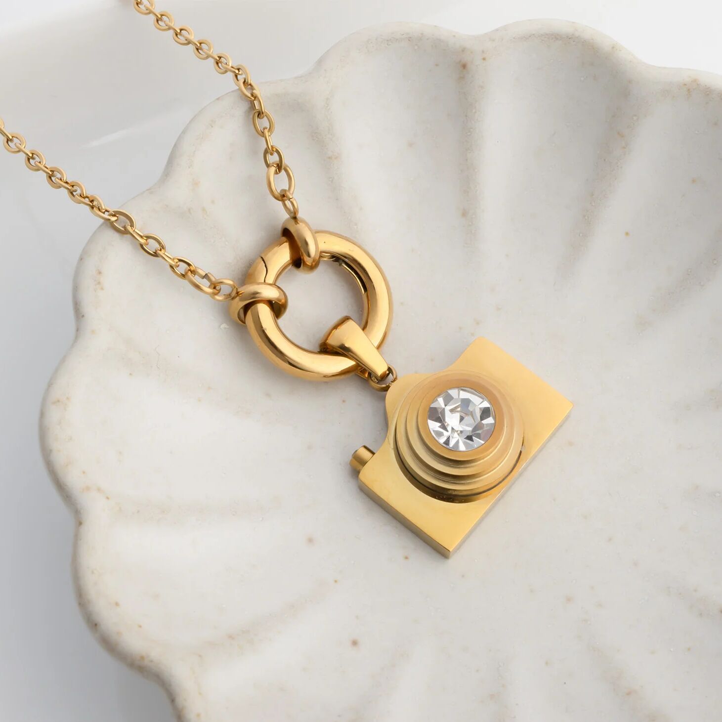 Gold camera-shaped pendant with a diamond on a marble surface