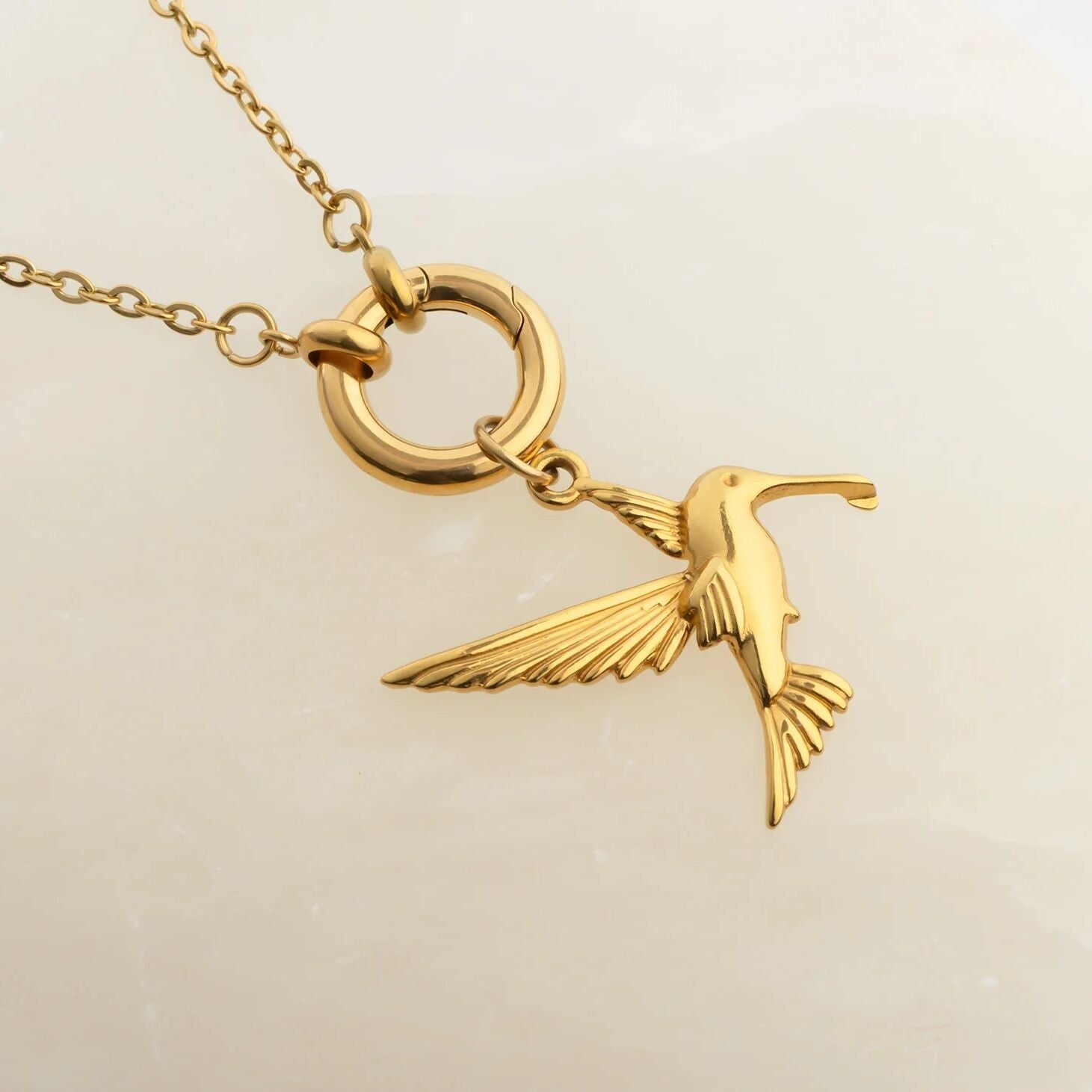 Gold bird pendant on a chain against a beige background
