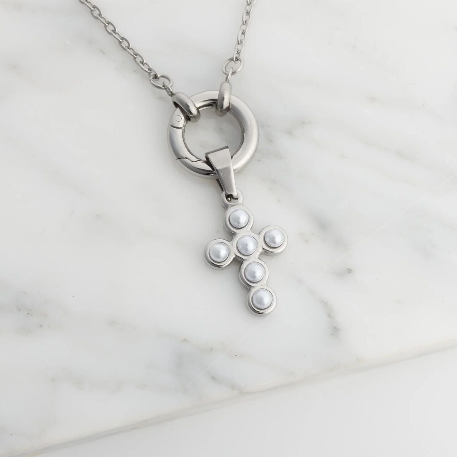 Silver cross necklace with pearl-like beads on a marble surface