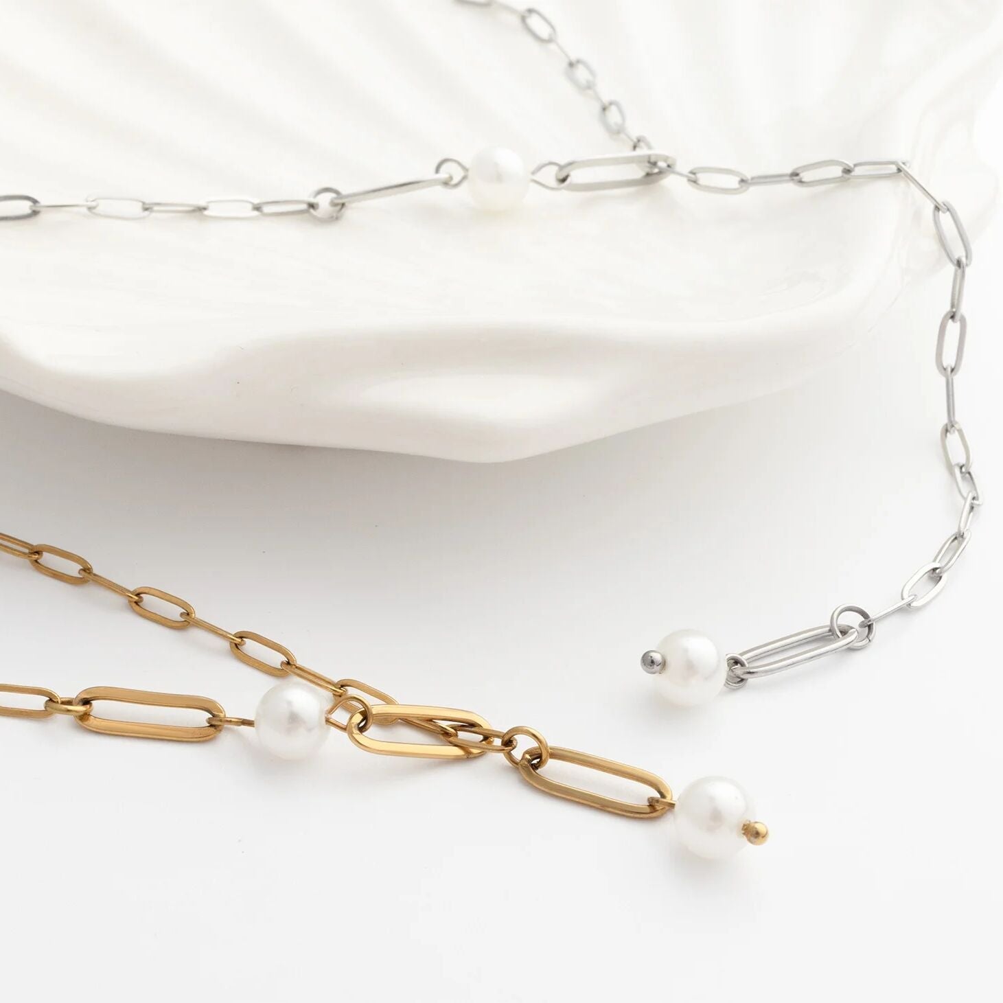 Two necklaces, one gold and one silver, with pearl accents on a white background.
