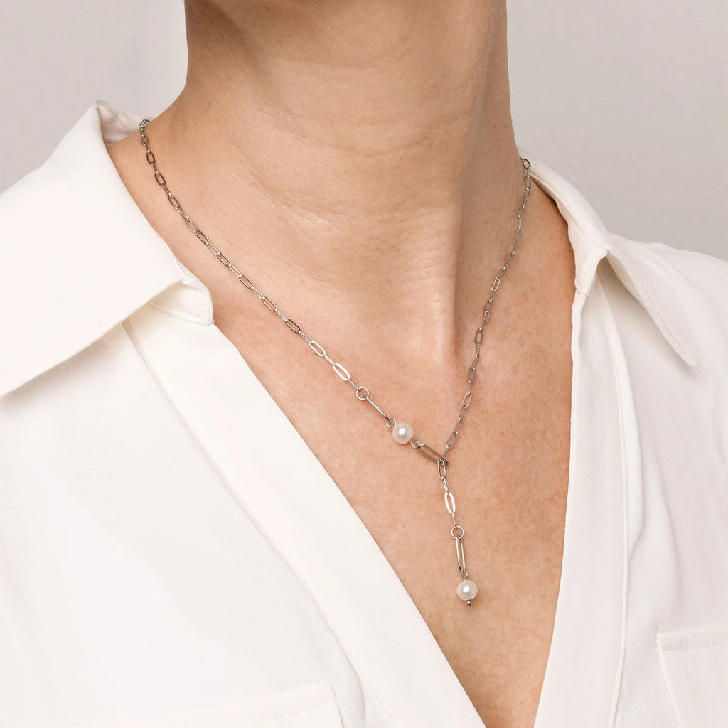Necklace with pearl pendant worn by a person in a white shirt against a neutral background