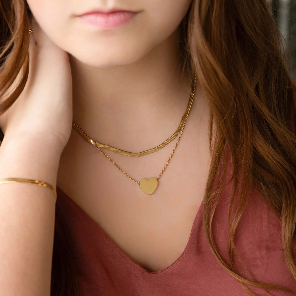 Close-up of a person wearing a gold heart-shaped necklace and bracelet.