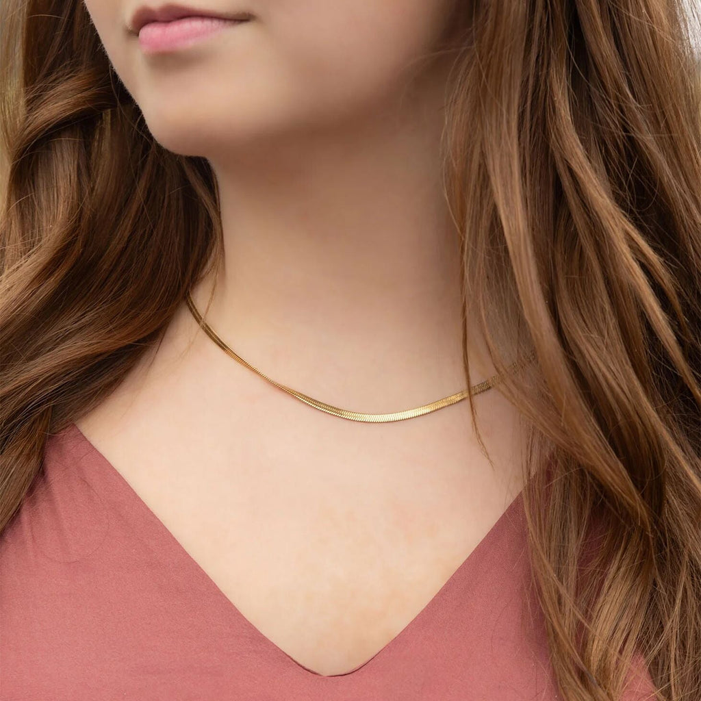 Close-up of a person wearing a gold necklace with long brown hair.