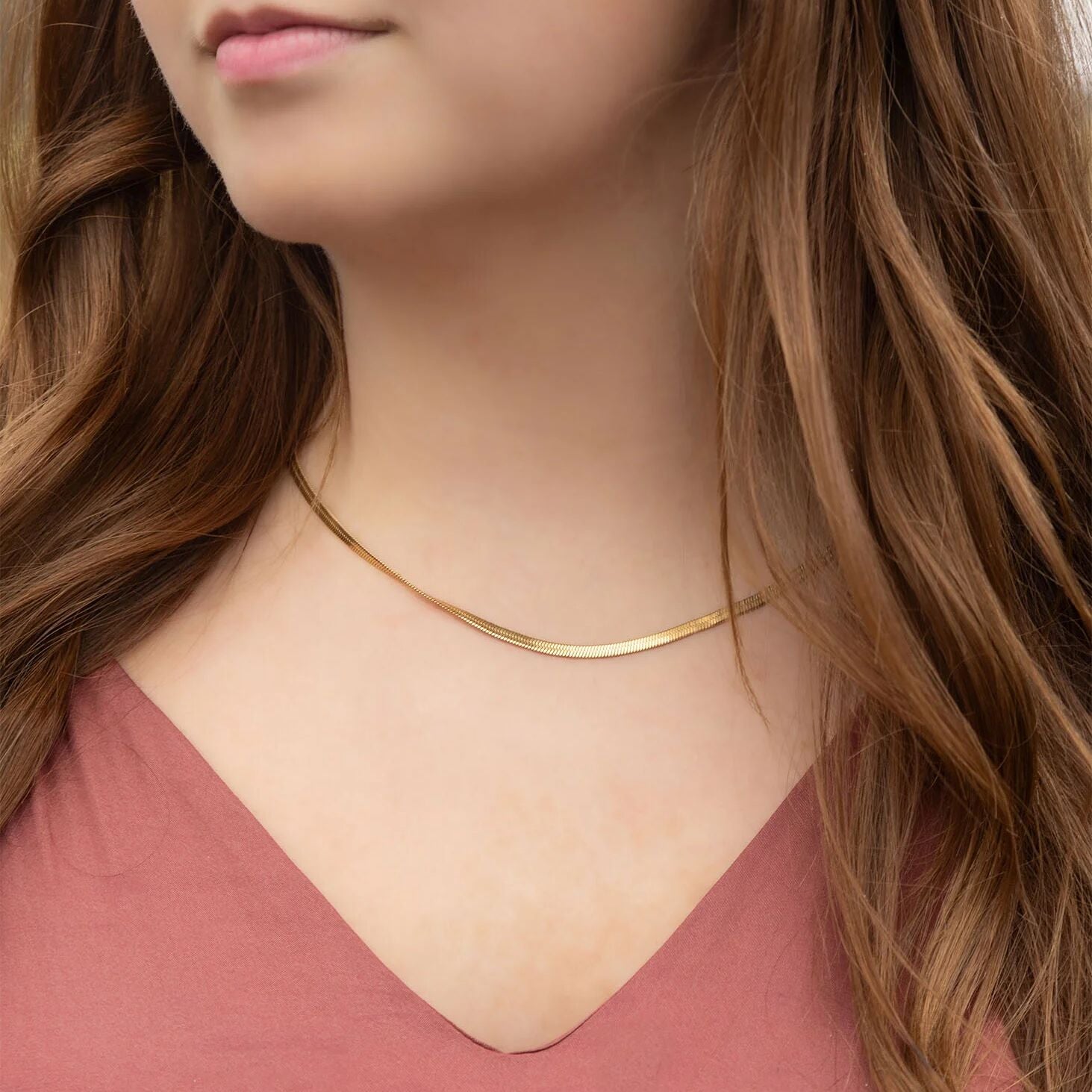 Close-up of a person wearing a gold necklace with long brown hair.