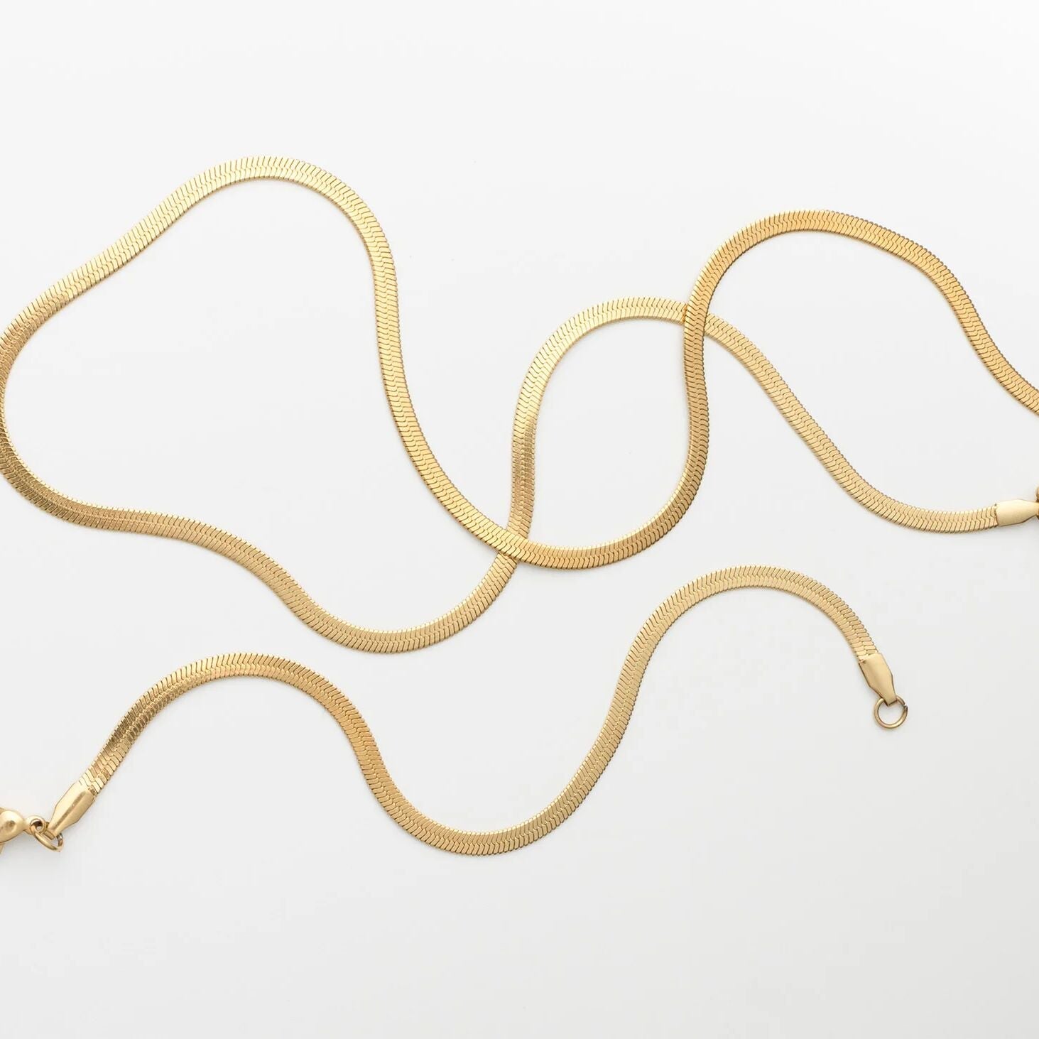 Gold snake chain necklace on a light gray background