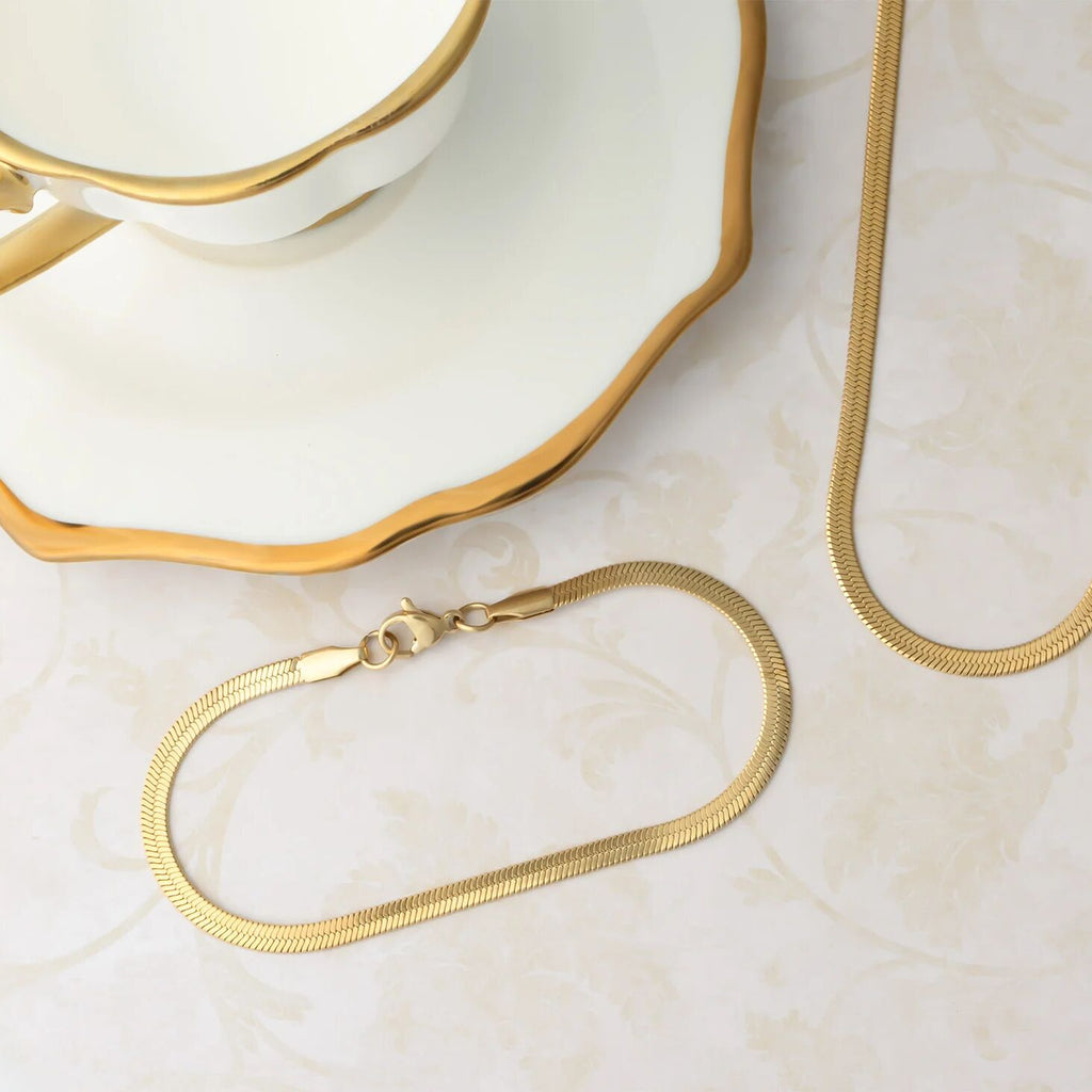 Gold necklace on a marble surface with a decorative dish in the background