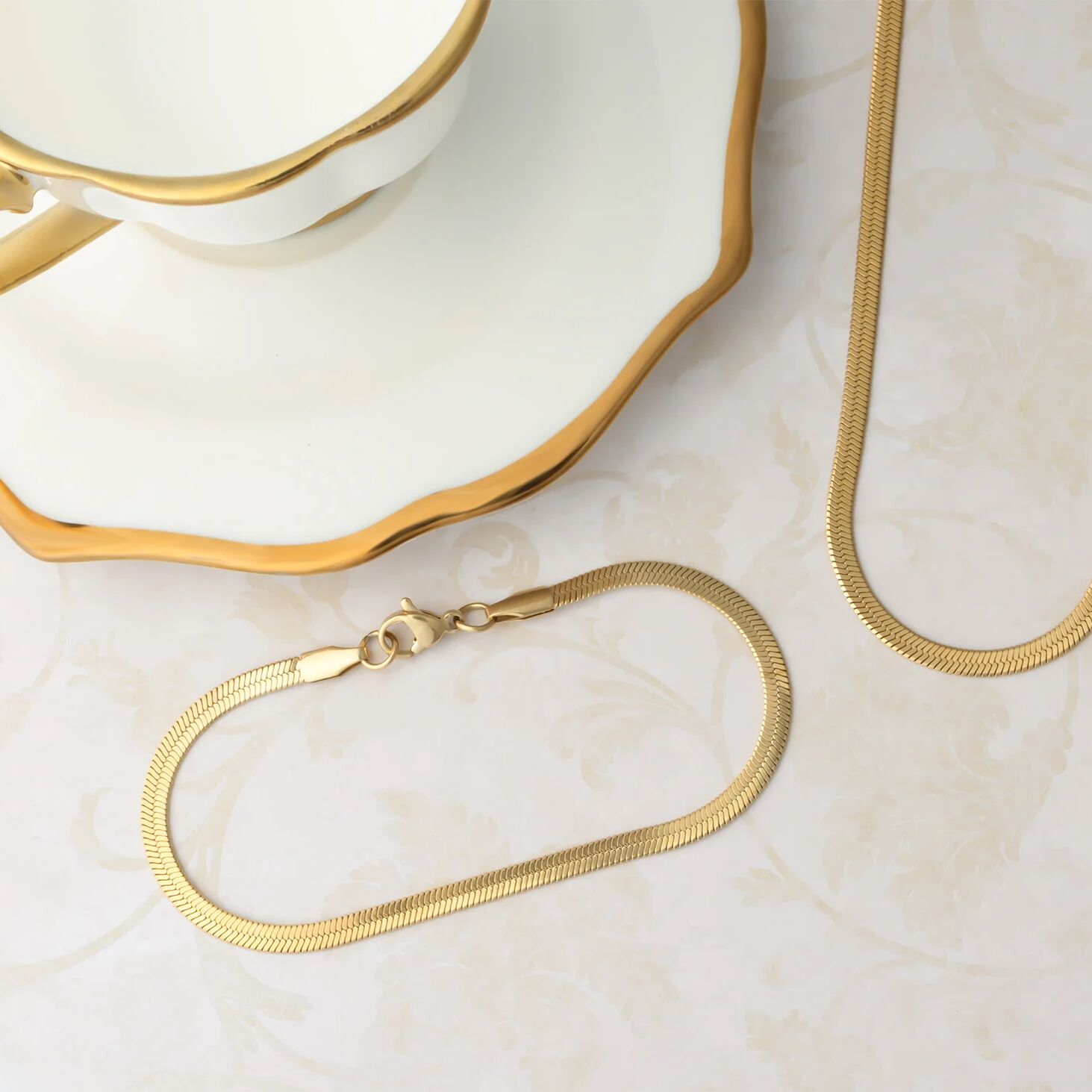 Gold necklace on a marble surface with a decorative dish in the background
