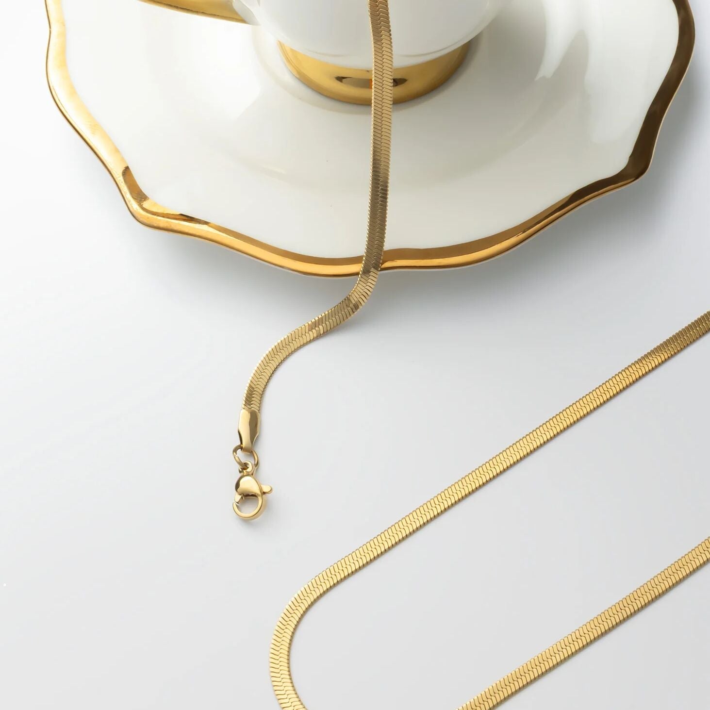 Gold necklace on a white surface with a cup and saucer in the background