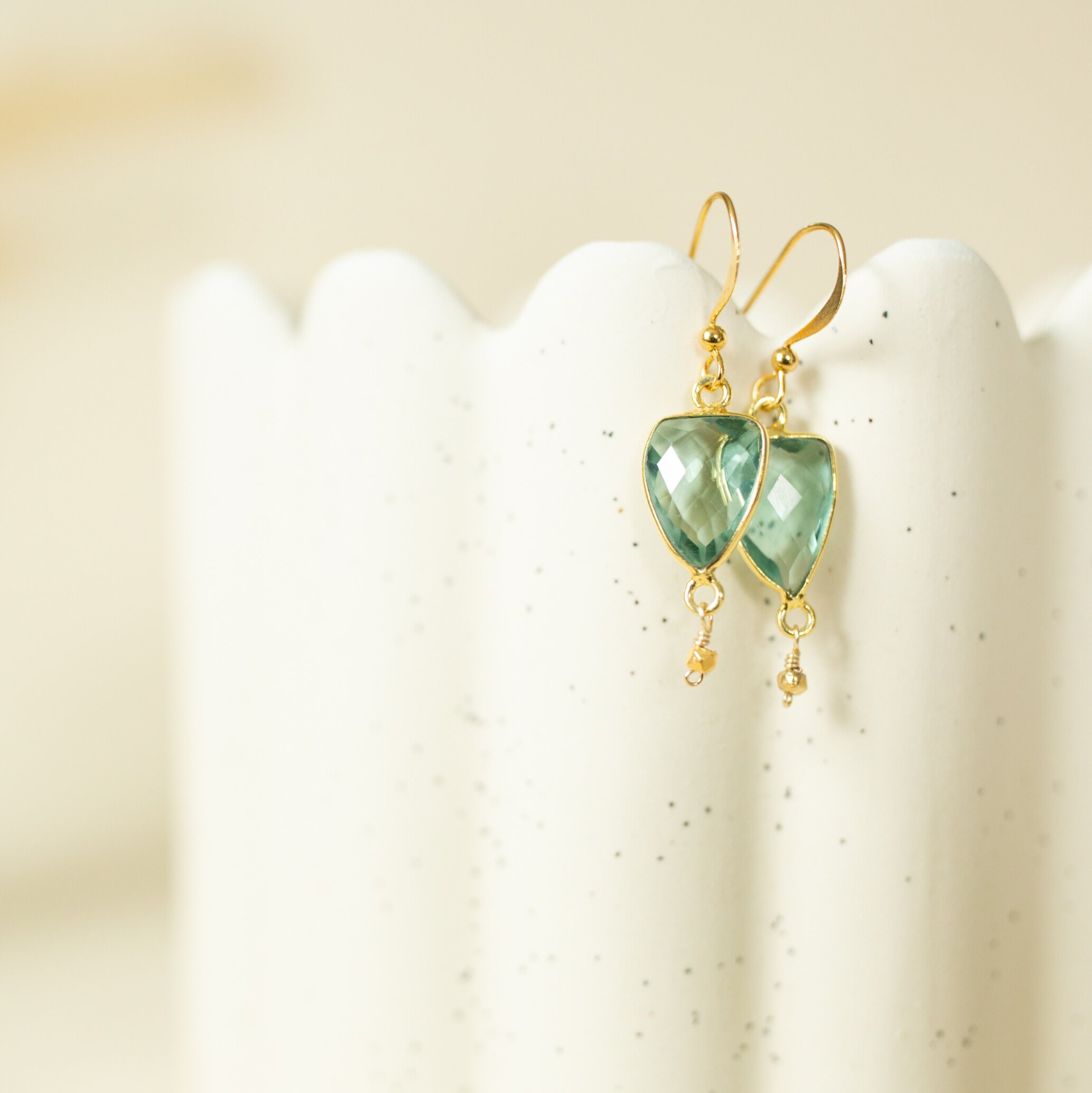 A pair of gold earrings with green gemstones hanging from the ear hooks.