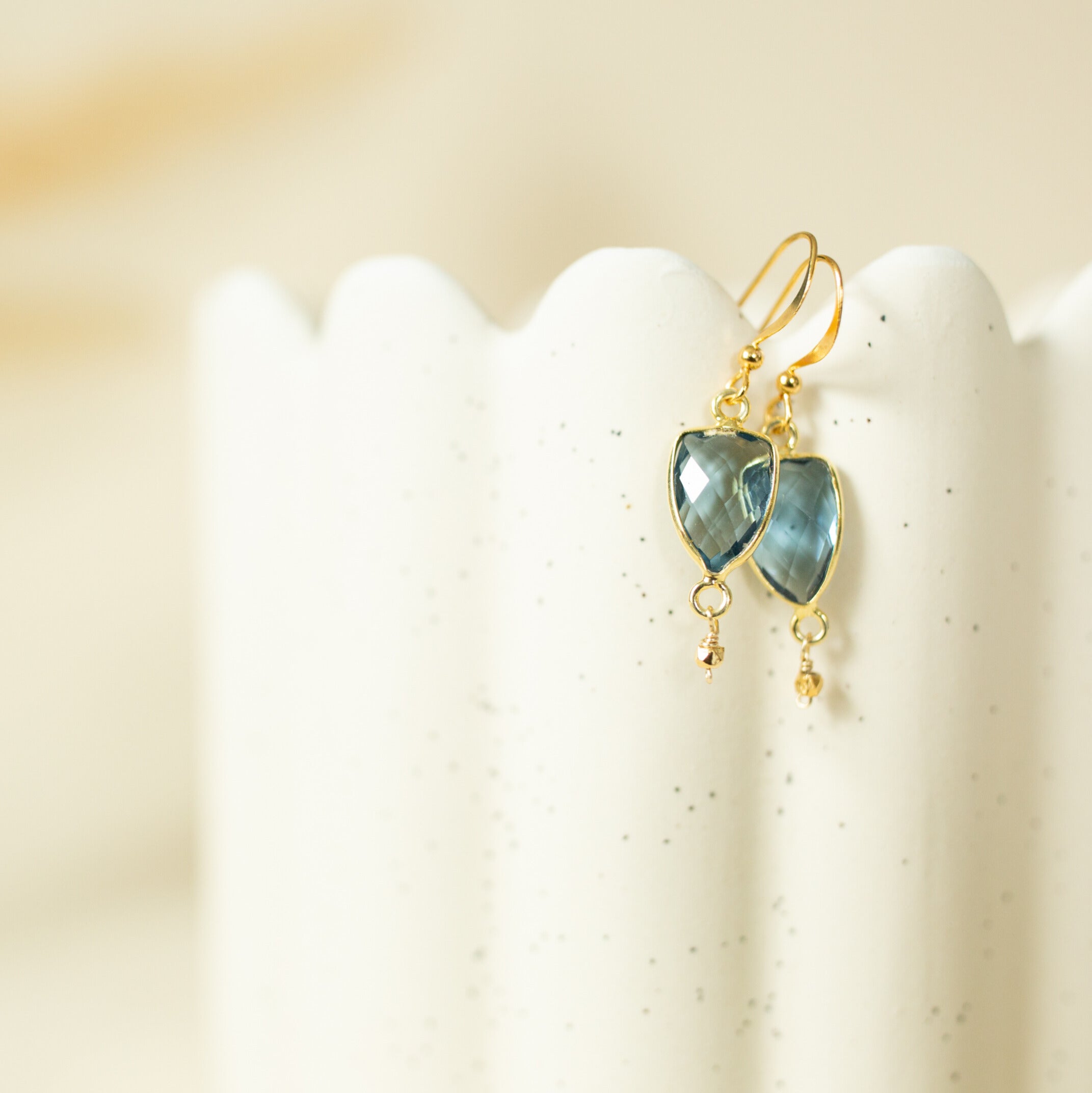 A pair of gold earrings with blue gemstones is displayed on a white vase.
